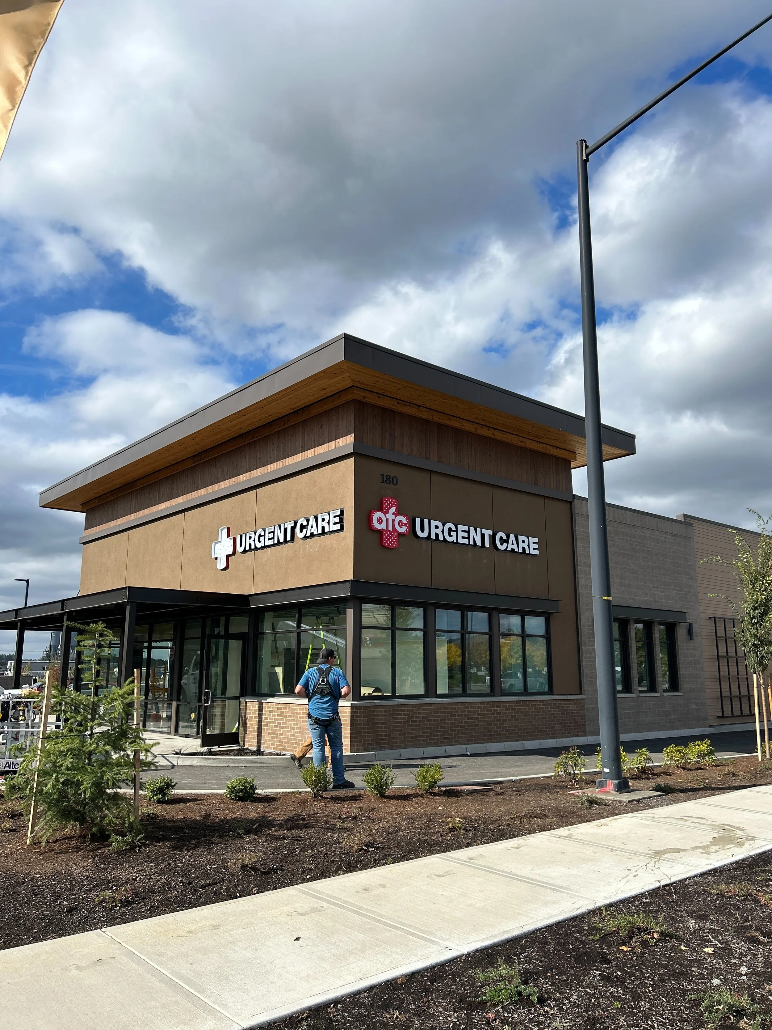 New building for AFC Urgent Care with signage, glass windows, and landscaping outside under a cloudy sky.