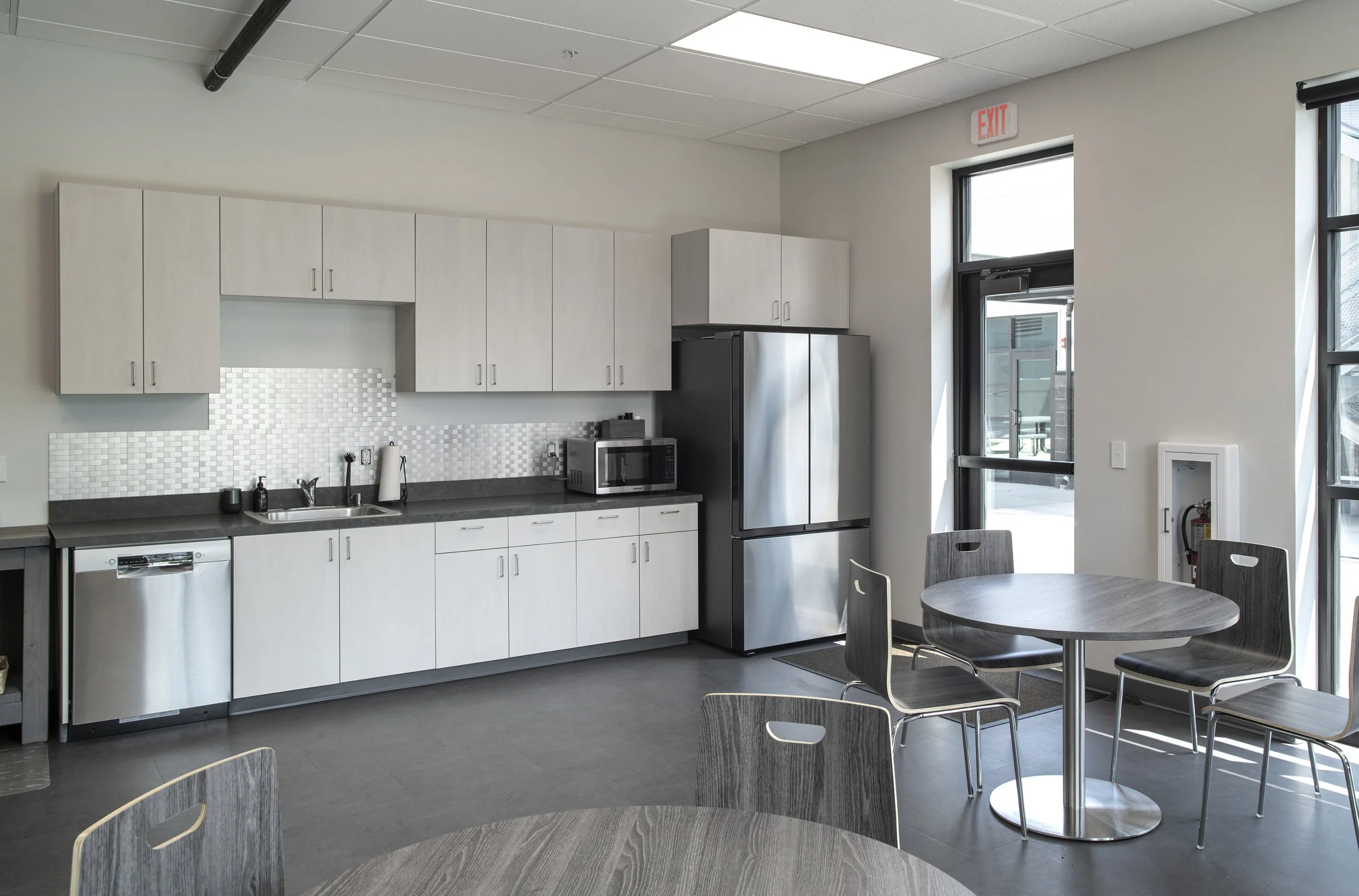 Modern kitchenette and dining area with gray cabinets, stainless steel appliances, and a round table with four chairs.