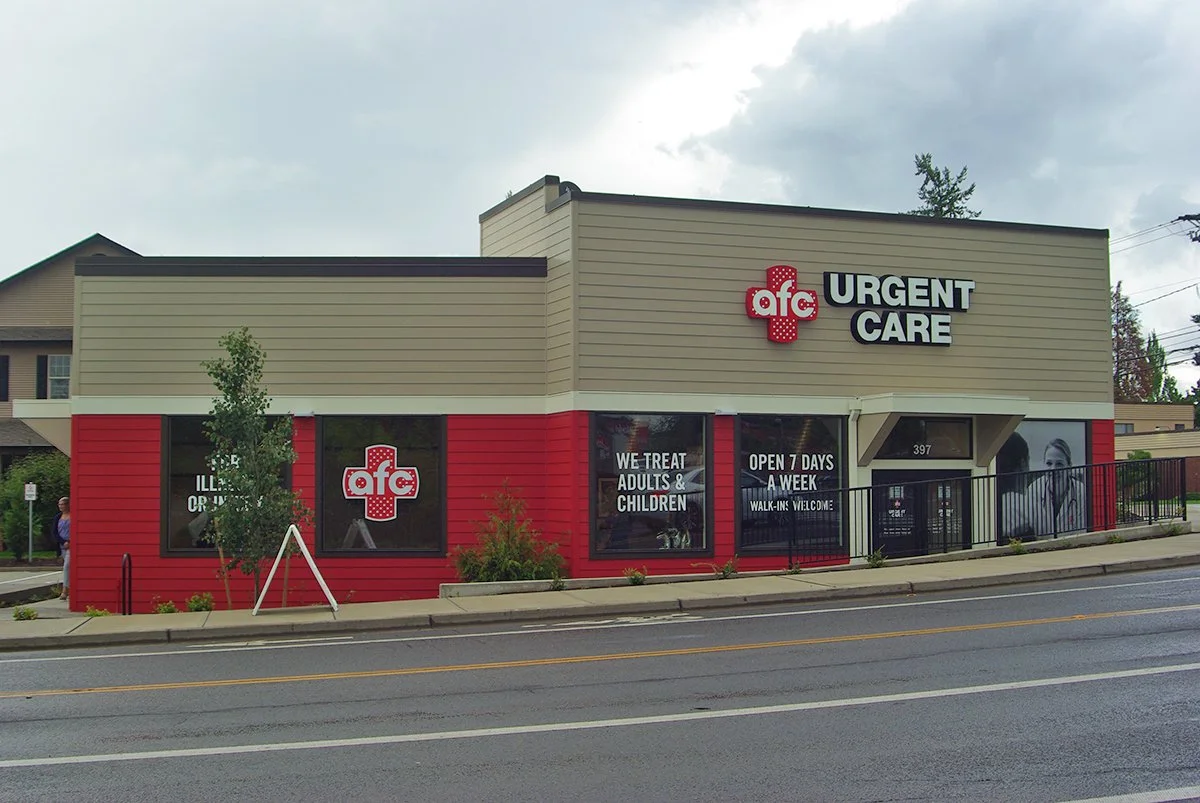 A medical clinic building with a sign that reads 'AFC Urgent Care' and windows displaying 'We treat adults and children,' 'Open 7 days a week,' and 'Walk-ins welcome.'