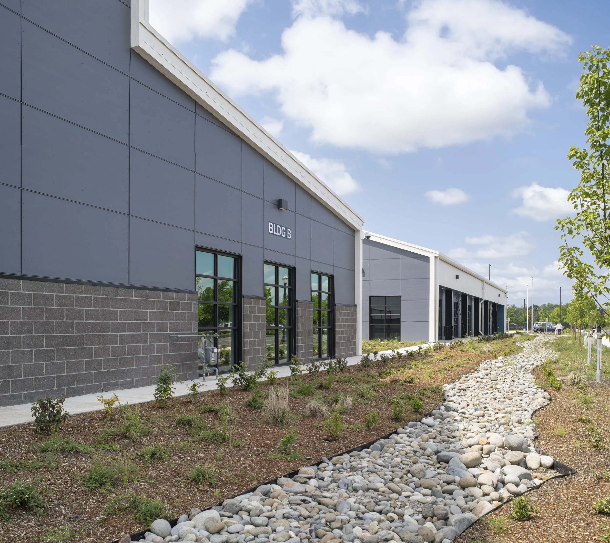 Modern industrial building with a dry riverbed landscape and young trees.