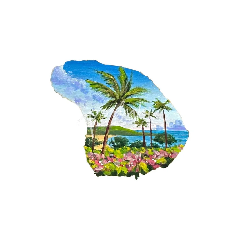 A hand-painted magnet in the shape of Lanai featuring five palm trees, pink flowers and the ocean in the background.