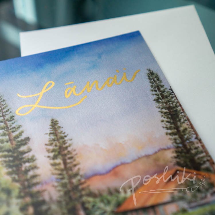 A close-up of a watercolor greeting card of pine trees and a plantation home on Lanai. The word "Lānaʻi" is handwritten in metallic gold ink.