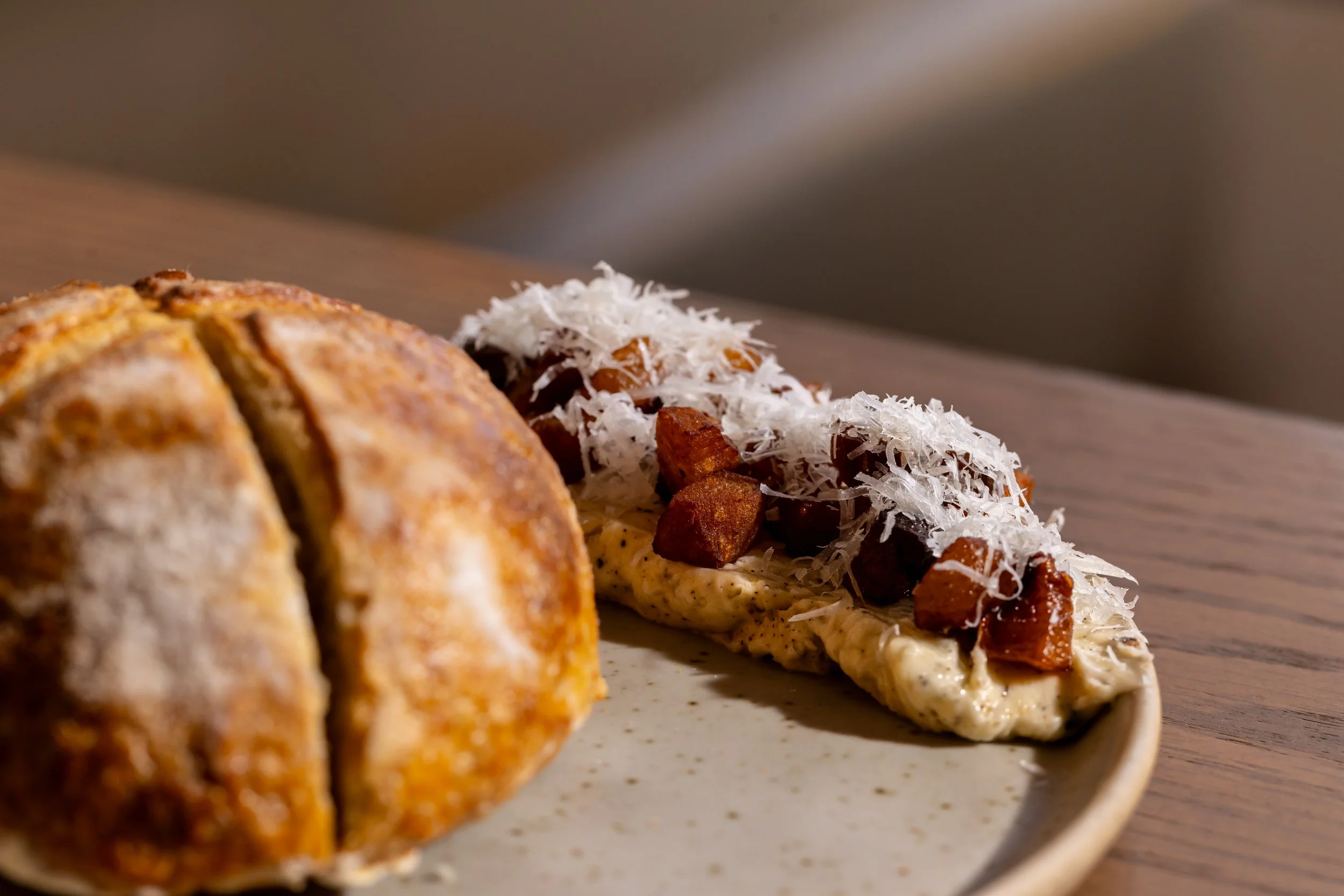 Sliced loaf of housemade sourdough bread and a serving of carbonara butter on a ceramic plate.