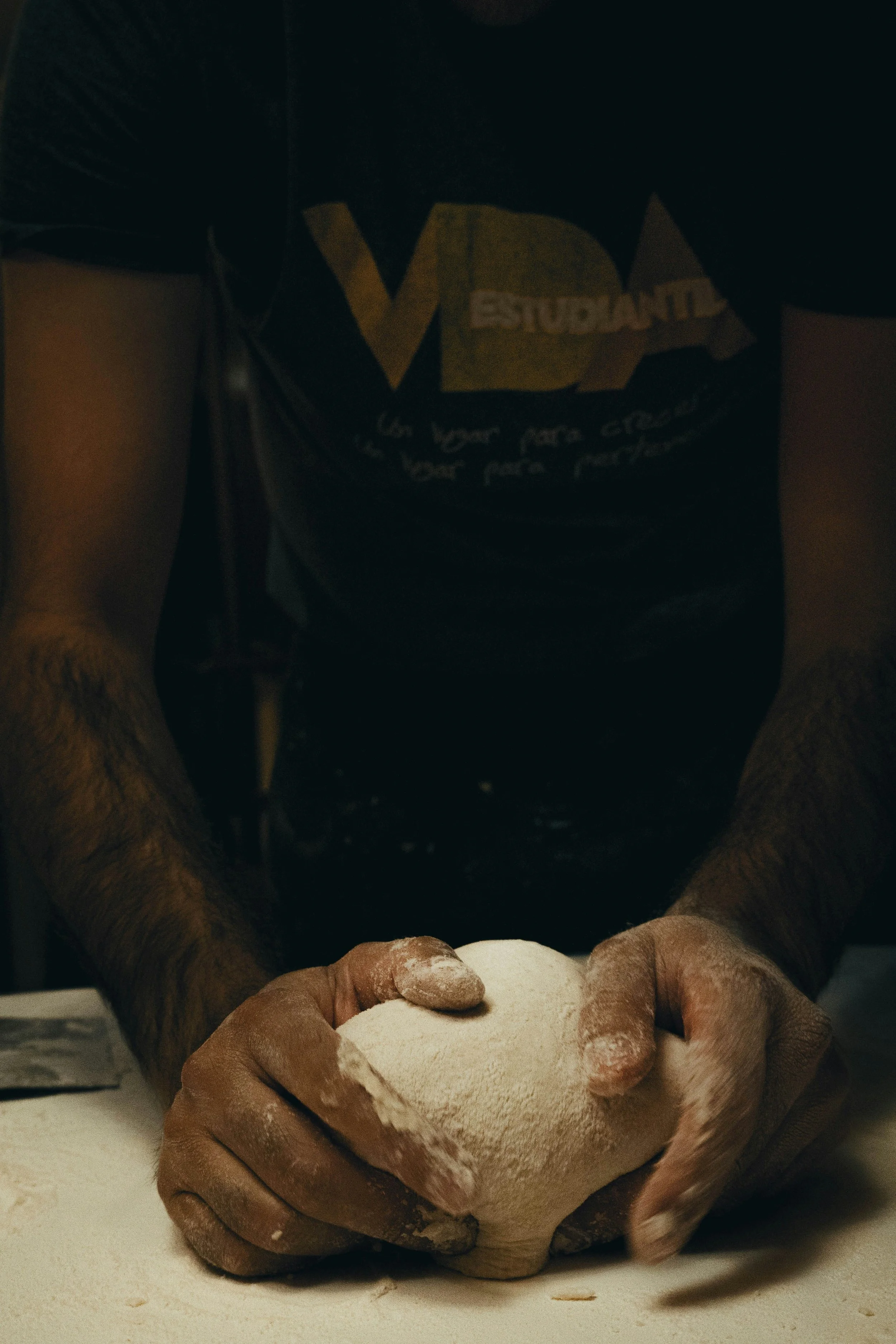 Person kneading dough on a floured surface with hands covered in flour