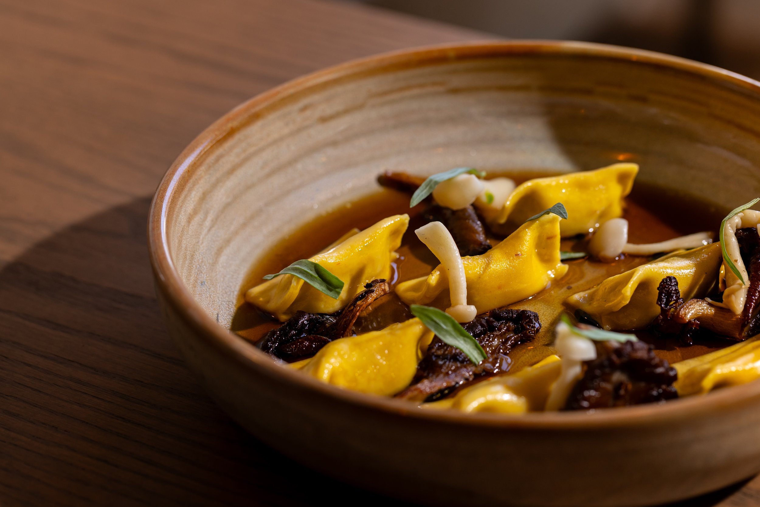 A ceramic bowl containing agnolotti on a wooden surface.