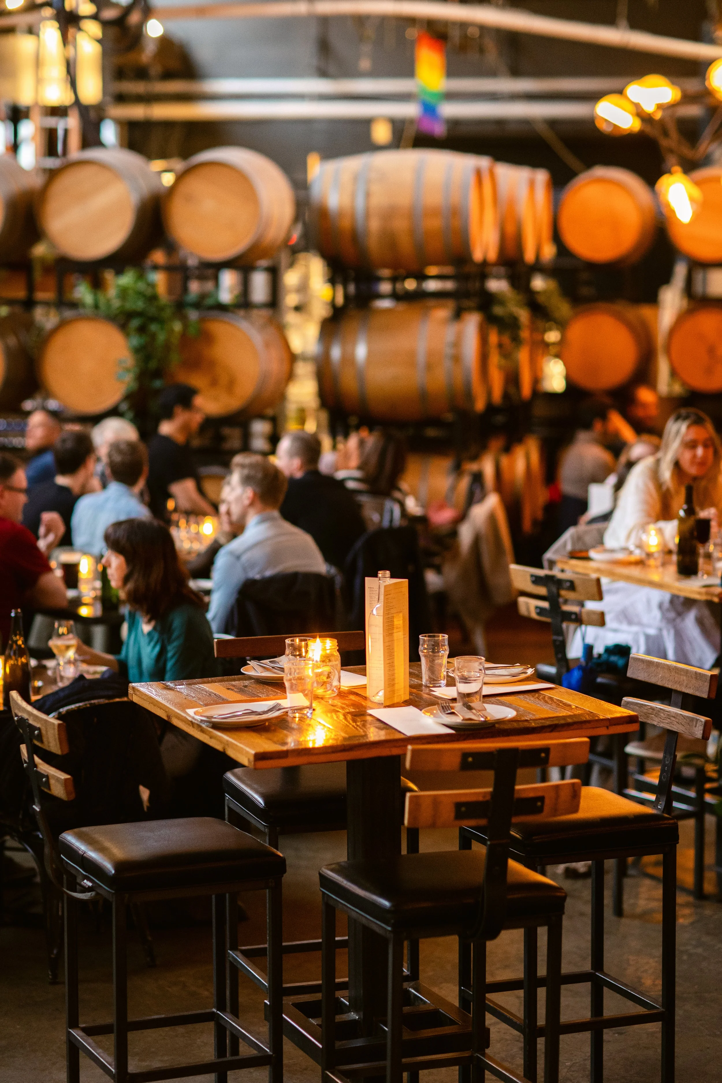 Belgard Kitchen, a lively restaurant with wooden tables, chairs, and wine barrels hanging on the wall, filled with people dining and talking. Warm lighting and a cozy atmosphere.