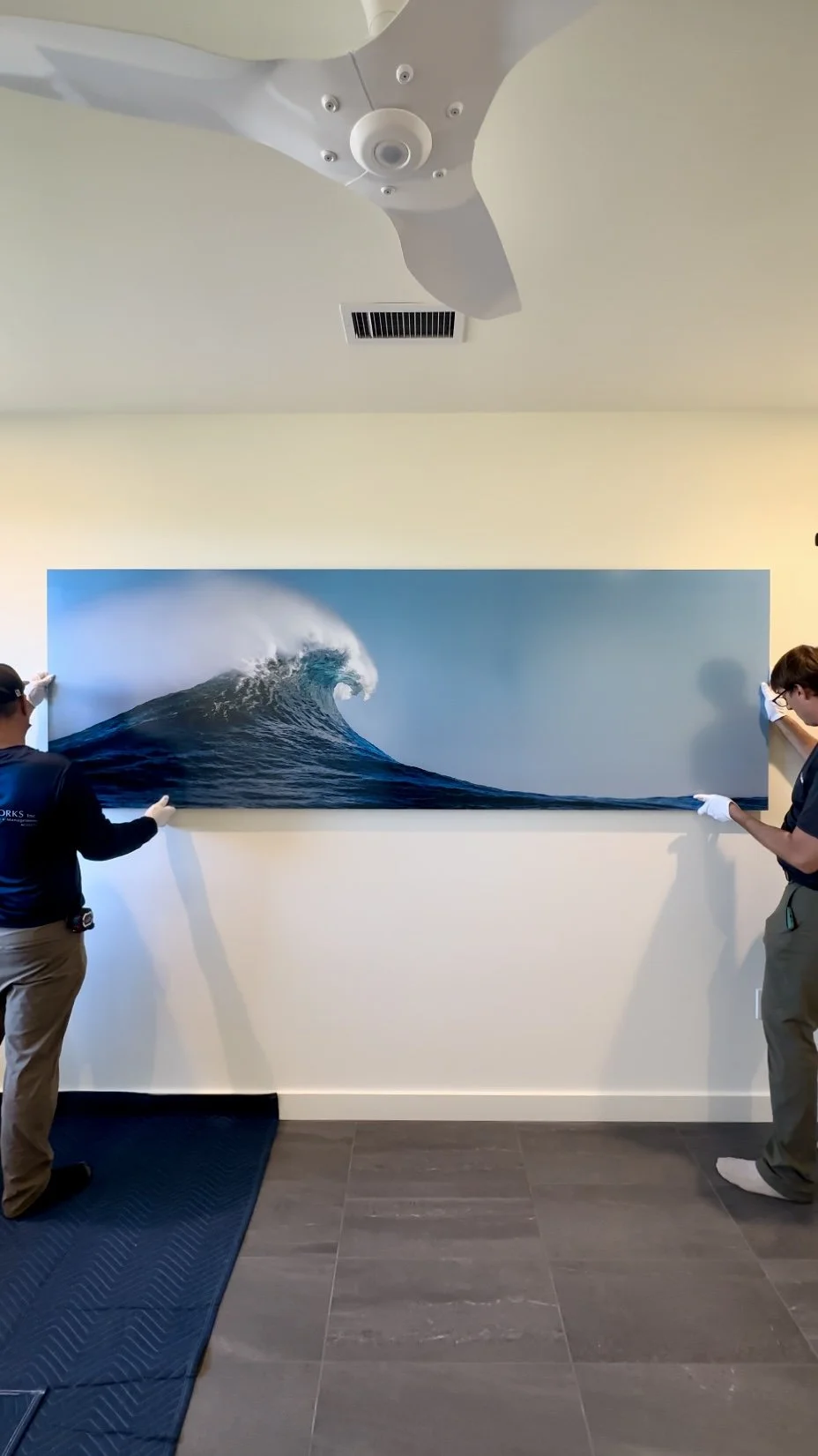 A huge panoramic fine art photography print of a beautiful wave being installed by two men with white gloves