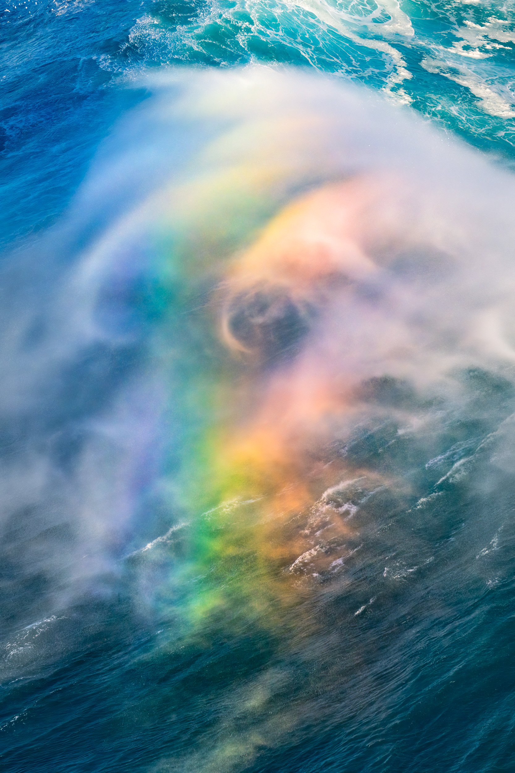 A rainbow illuminating in the spraying mist from a rogue ocean wave on Maui's north shore.