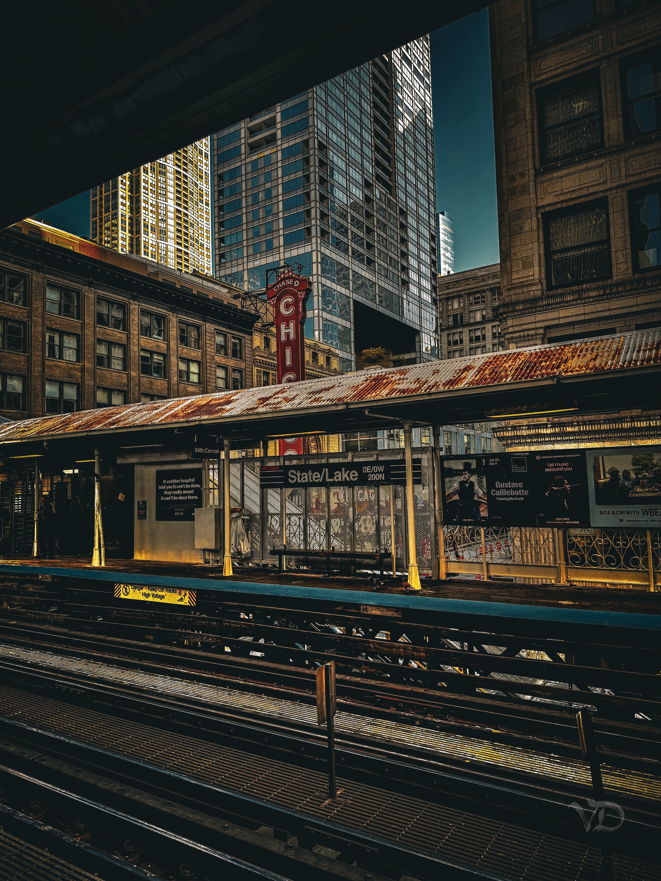 Empty subway station platform at State/Lake station with tracks, a train door and shadows, surrounded by tall buildings in a city.