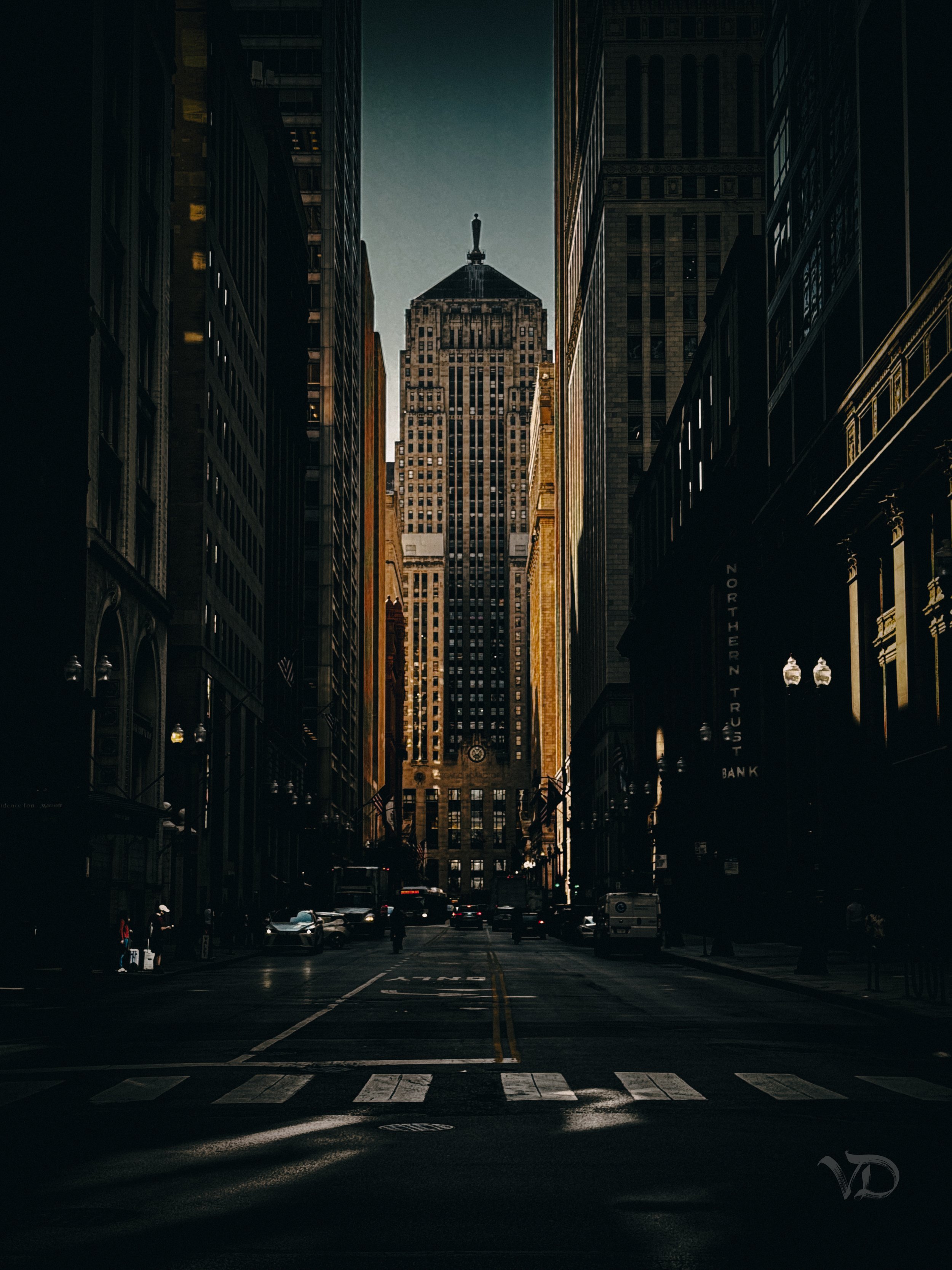 City street lined with tall buildings, with a prominent skyscraper in the background under a clear sky.