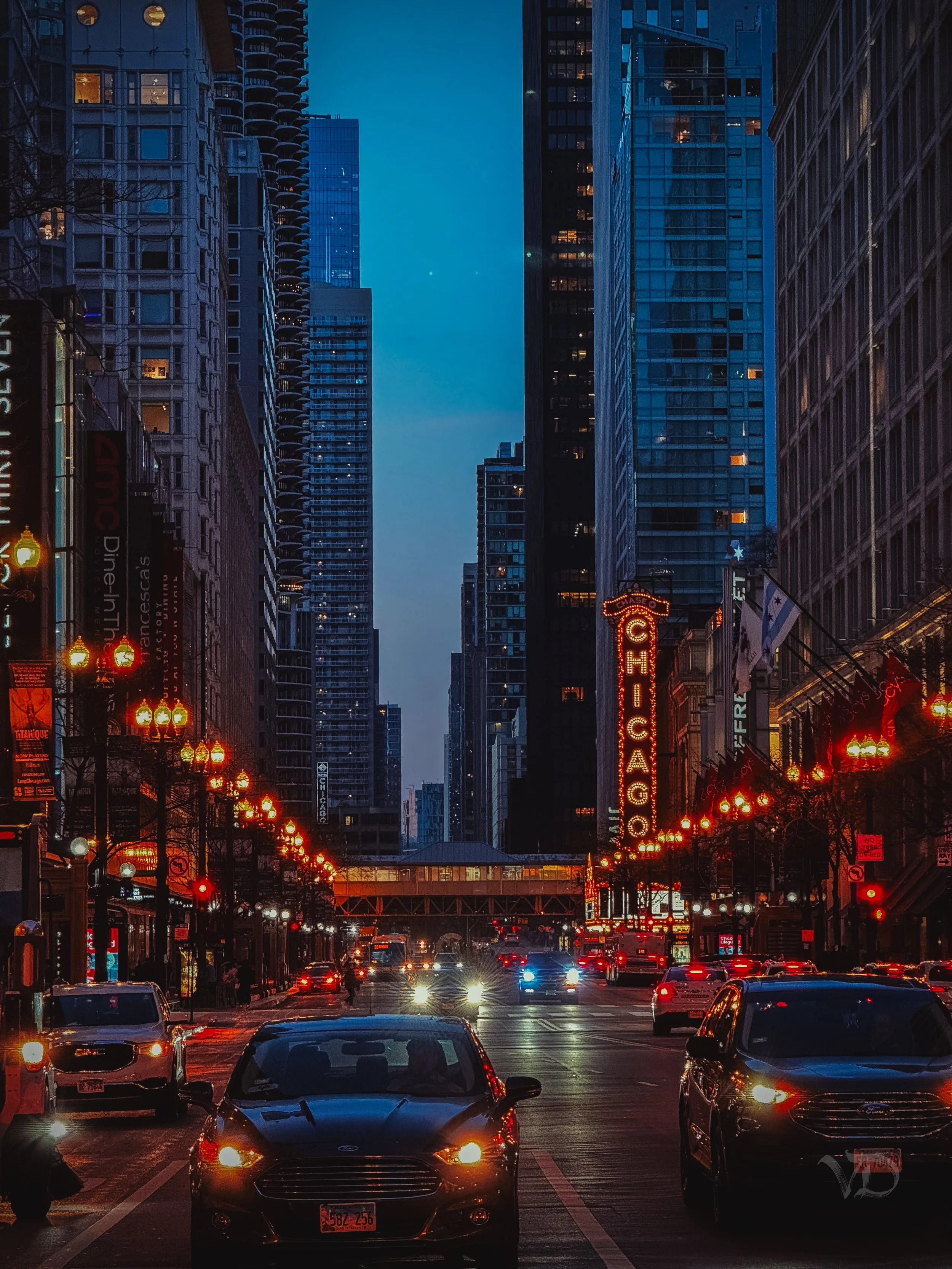 Nighttime street scene in Chicago with cars, illuminated streetlights, and the Chicago Theatre marquee sign in downtown Chicago.
