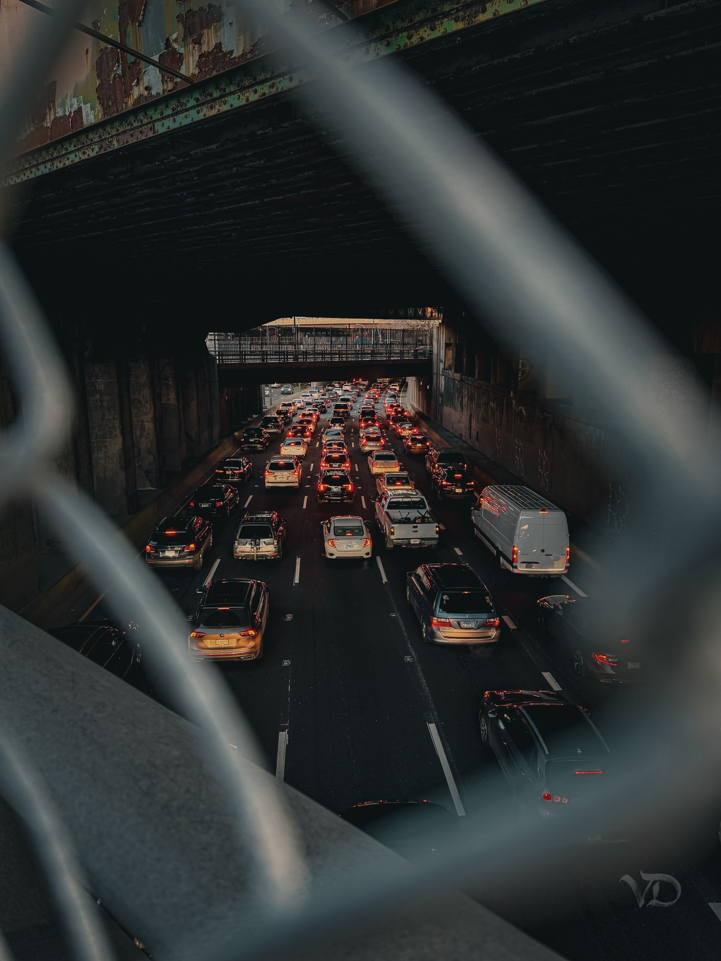 Traffic jam on a multi-lane highway viewed through a chain-link fence, during sunset or dusk.