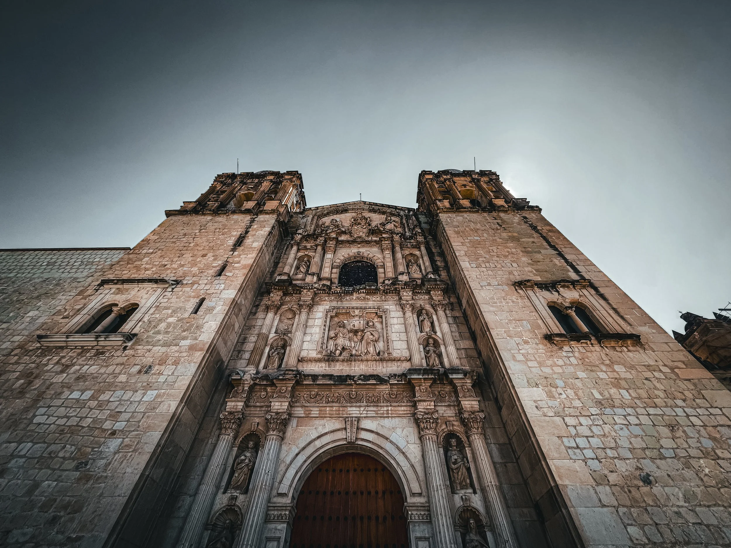 From a low angle, a historic stone cathedral with twin towers and ornate carvings on its facade, under a clear sky.