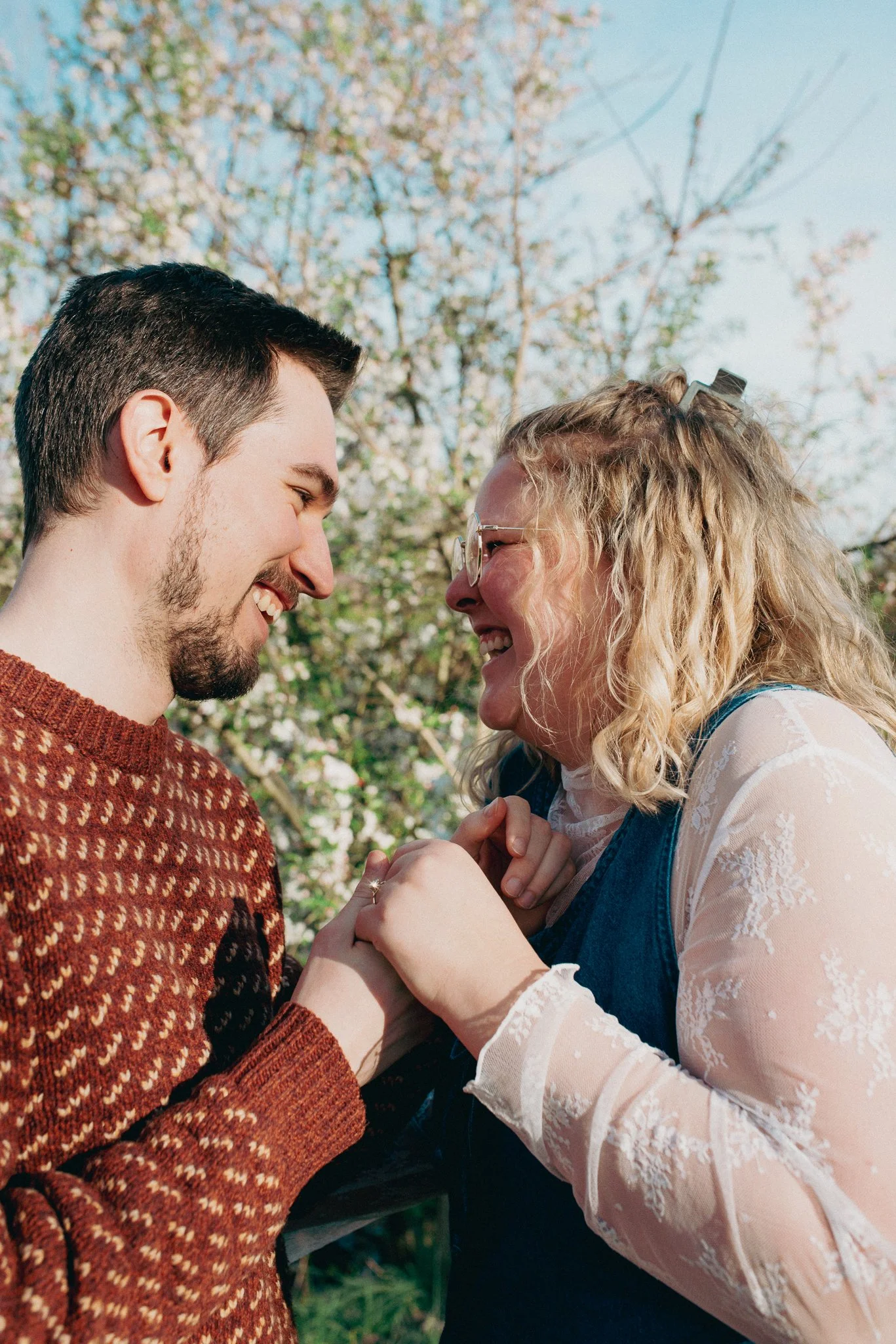 Engagement photoshoot of man and a woman smiling and holding hands outdoors, with trees and a clear sky in the background. Richmond, Indiana.