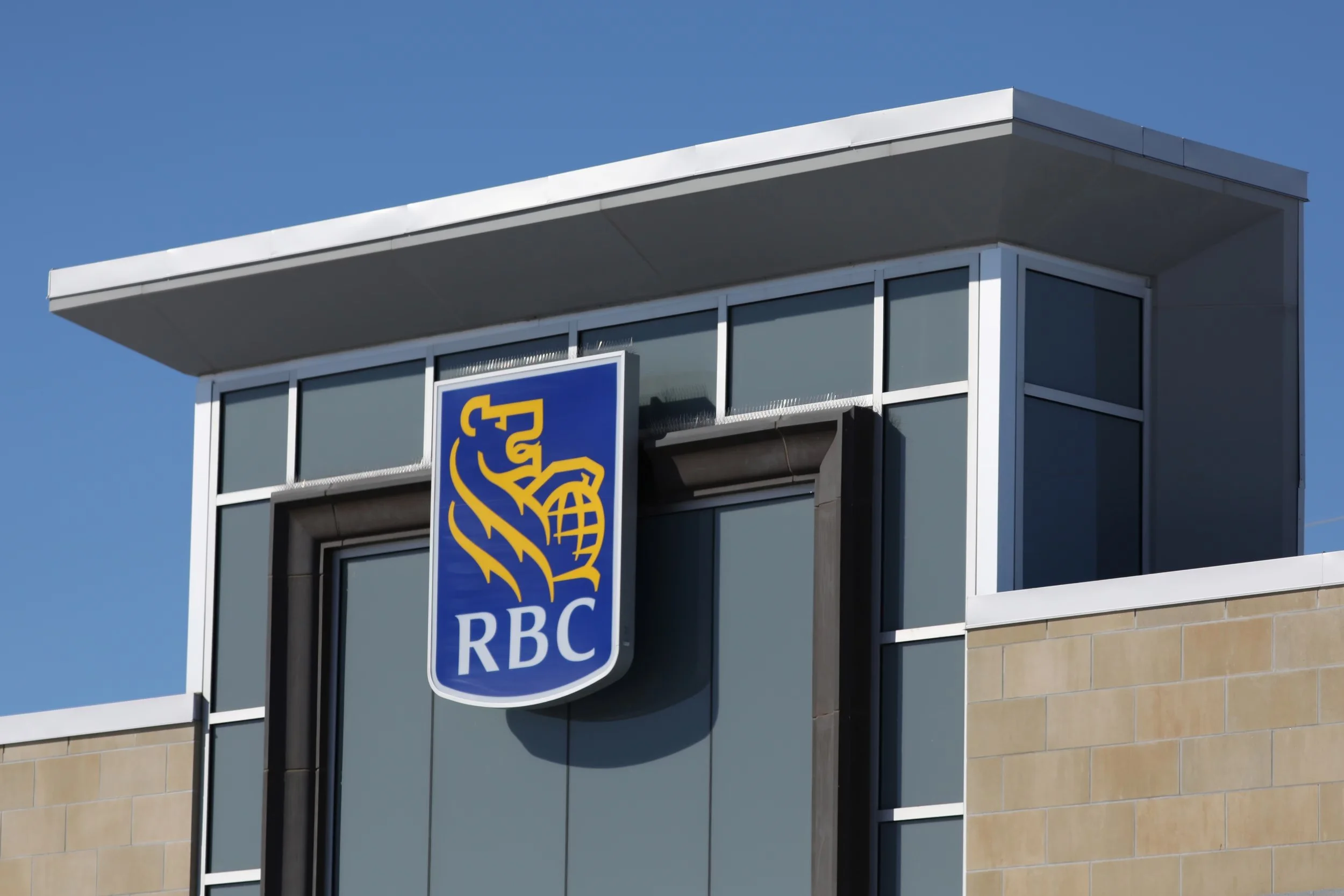 Close-up of a modern building facade with an RBC bank sign featuring a lion with a globe, against a blue sky.