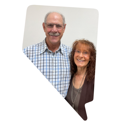 A smiling couple standing indoors against a plain white wall.