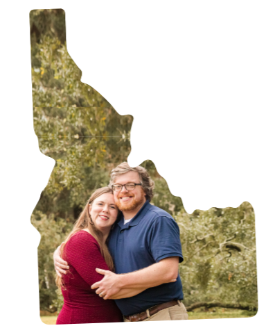A happy couple hugging outdoors in a park with trees in the background.
