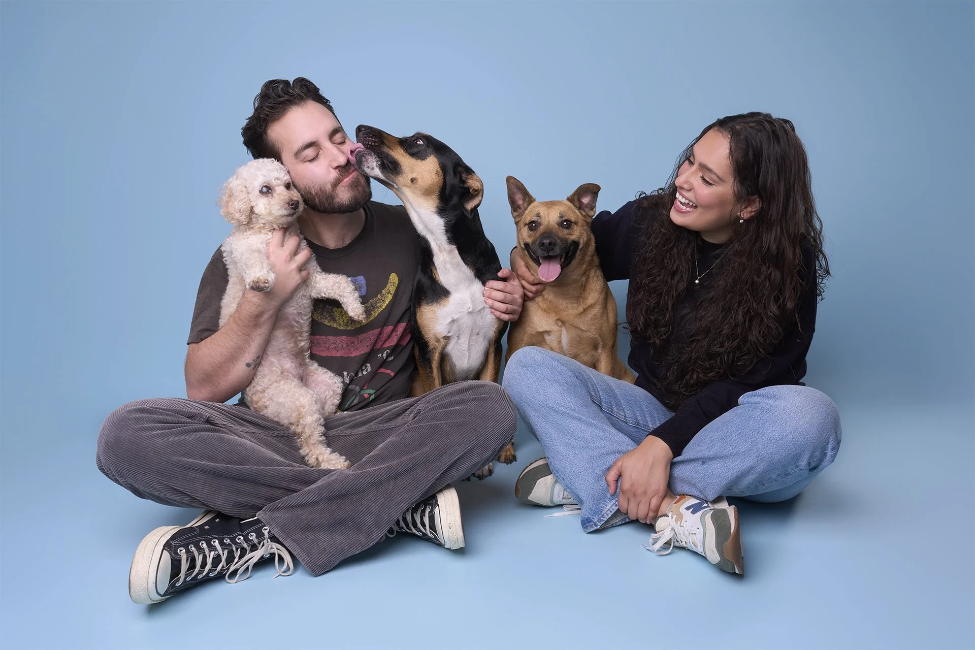 Portrait of three dogs and their family sitting and smiling on a light blue background at Los Angeles dog photography studio Shuttermutt Photo