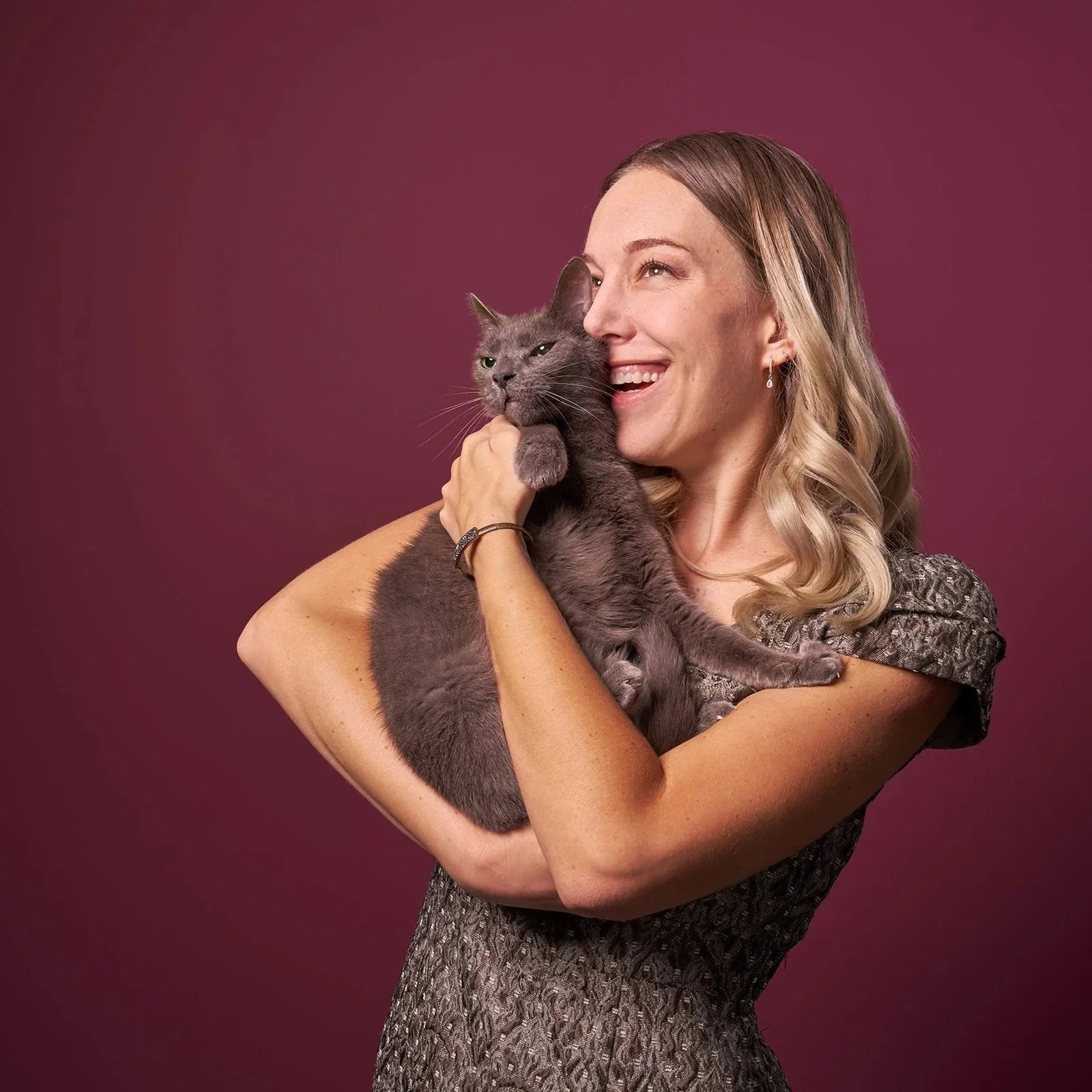  Photo of a woman smiling and holding her senior cat, both gazing to the left against a mauve background in LA photo studio 