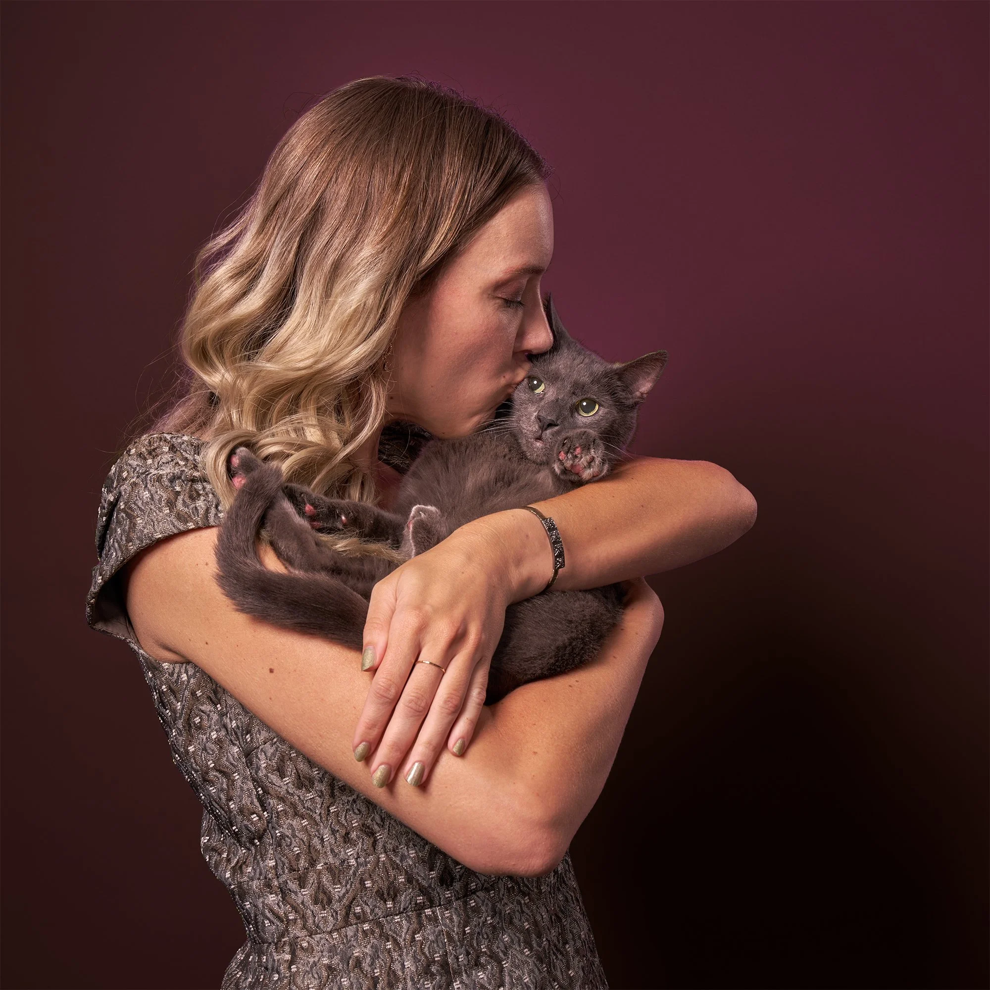  Photo of a woman in a dress holding her gray cat in her arms and kissing his head against a mauve background in Los Angeles  