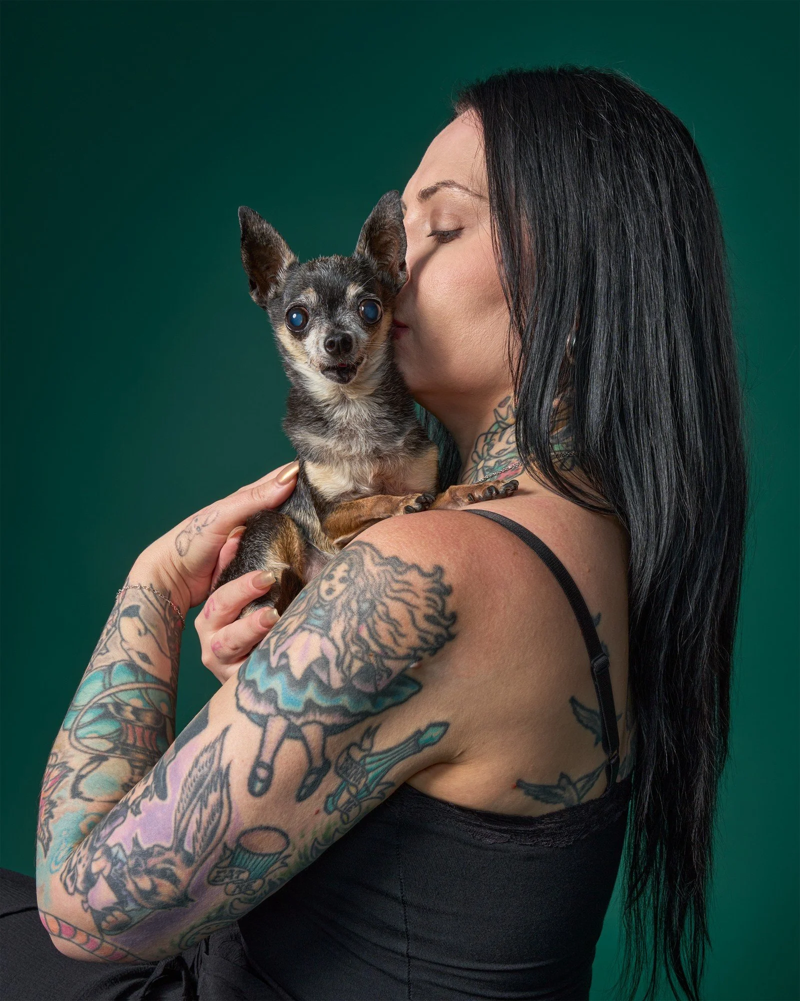 Woman with colorful tattoos holding a very small senior chihuahua on green background