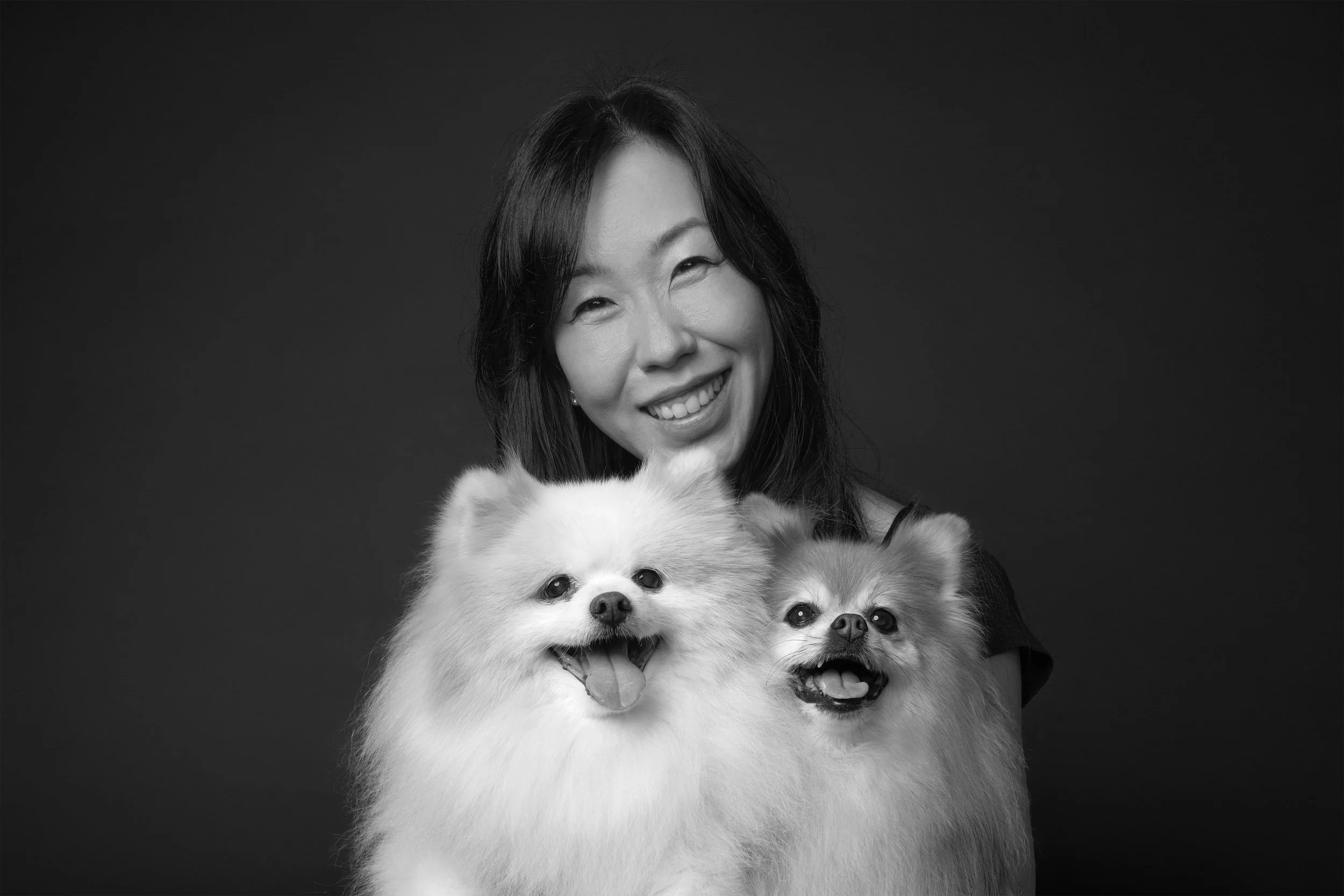 Black and white portrait of smiling woman holding two fluffy Pomeranian dogs in Los Angeles