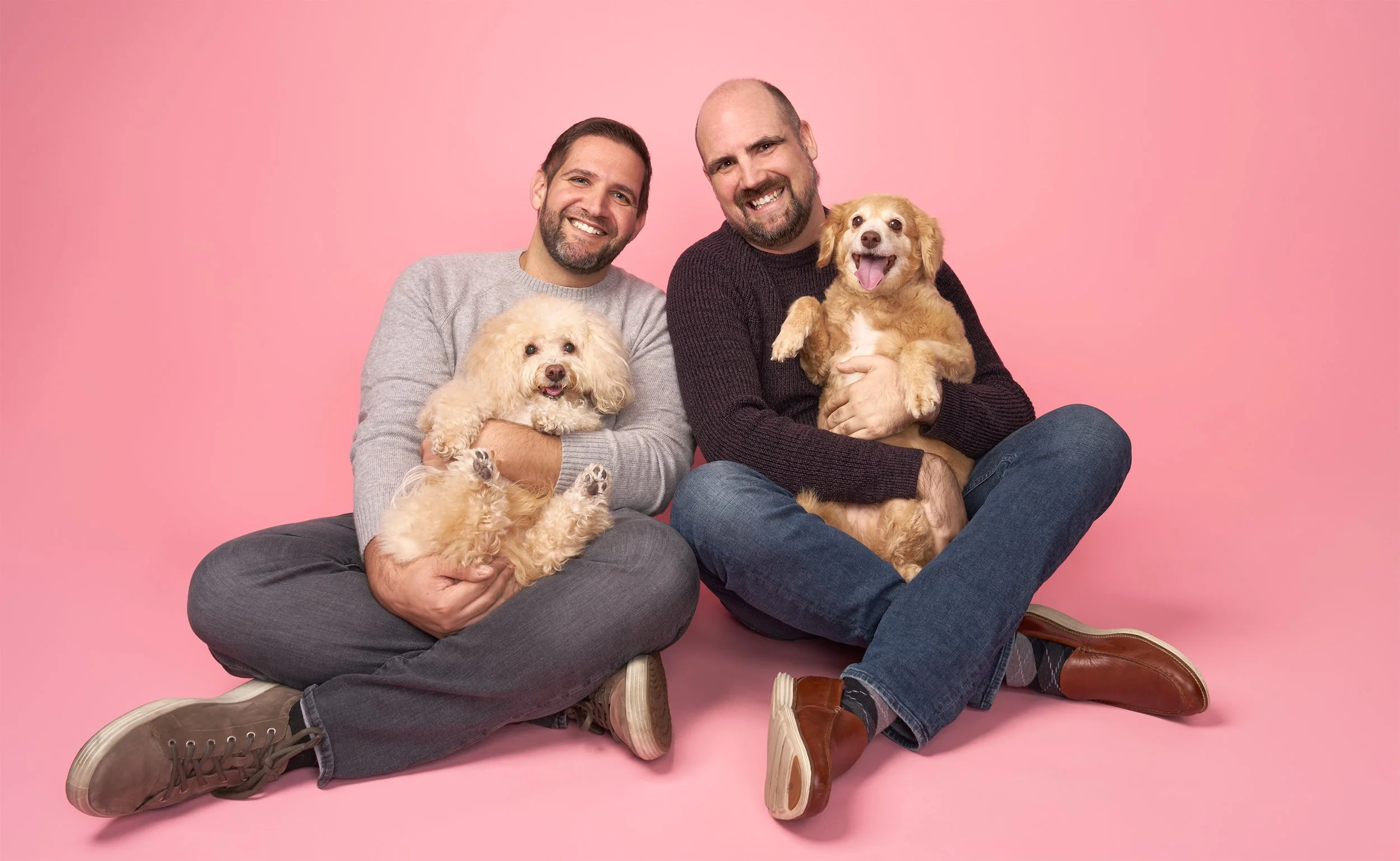 Smiling family of two men with two small, senior dogs on pink background in LA pet portrait studio