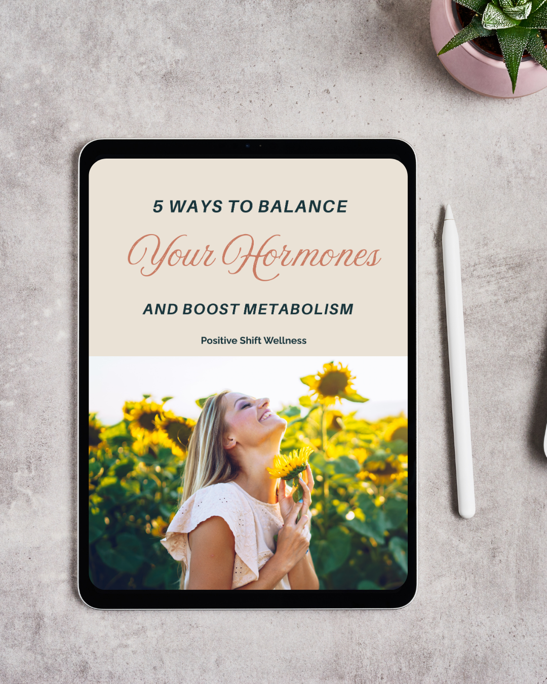 An iPad displaying a wellness guide titled '5 Ways to Balance Your Hormones and Boost Metabolism' with a photo of a woman in a sunflower field smiling and holding a sunflower, placed on a gray desk next to a white stylus and a potted plant in a pink pot.