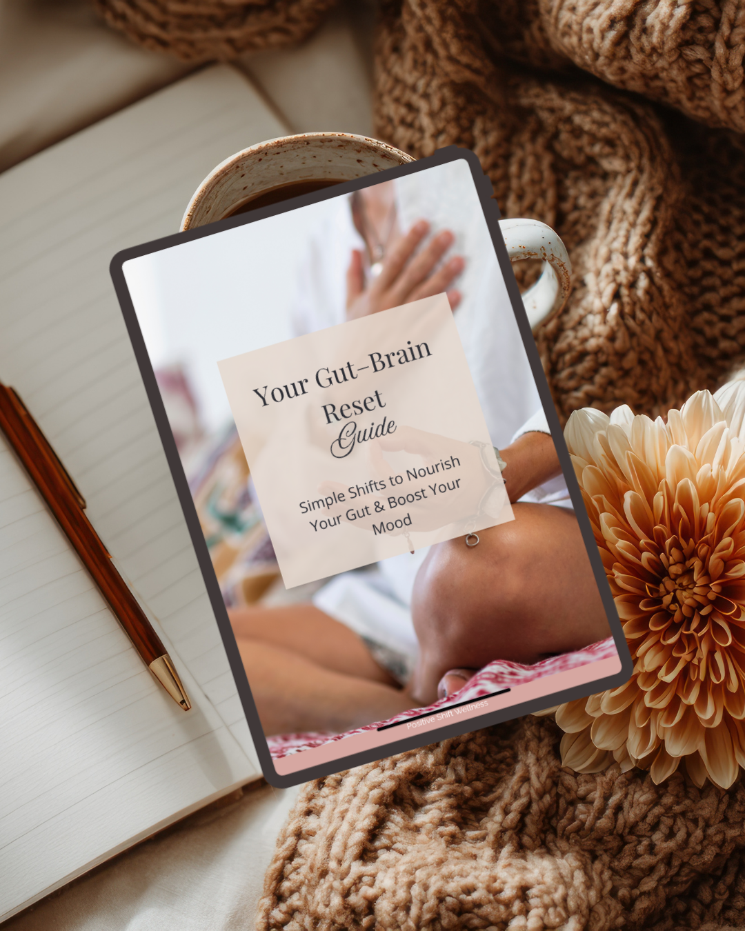 A tablet displaying a guide titled 'Your Gut-Brain Reset Guide' with a subtitle 'Simple Shifts to Nourish Your Gut & Boost Your Mood.' The tablet is placed on a cozy blanket, next to a notebook with a pen, a cup of coffee, and a peach-colored flower.