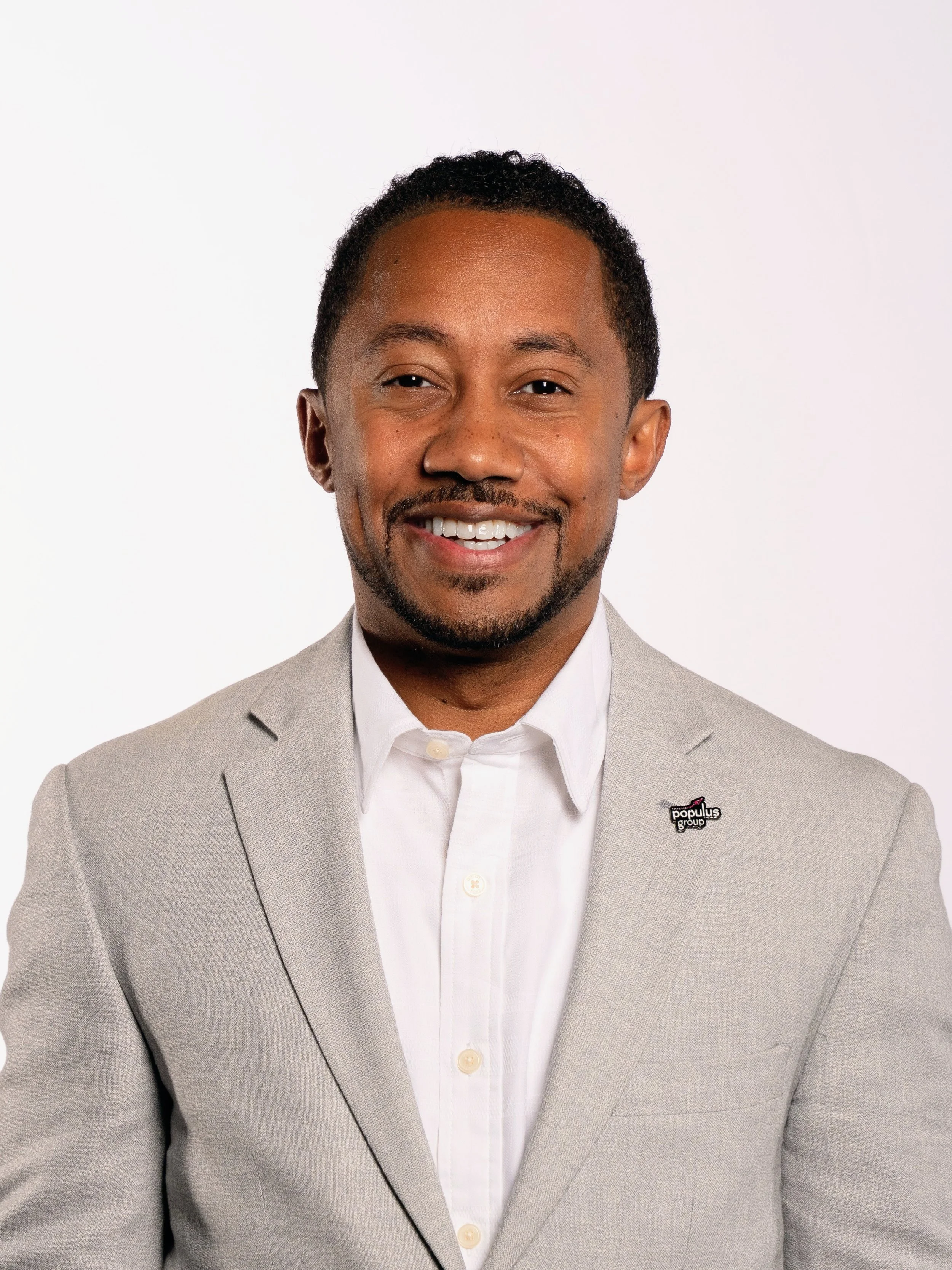 A smiling man in a light gray suit and white shirt standing against a white background.