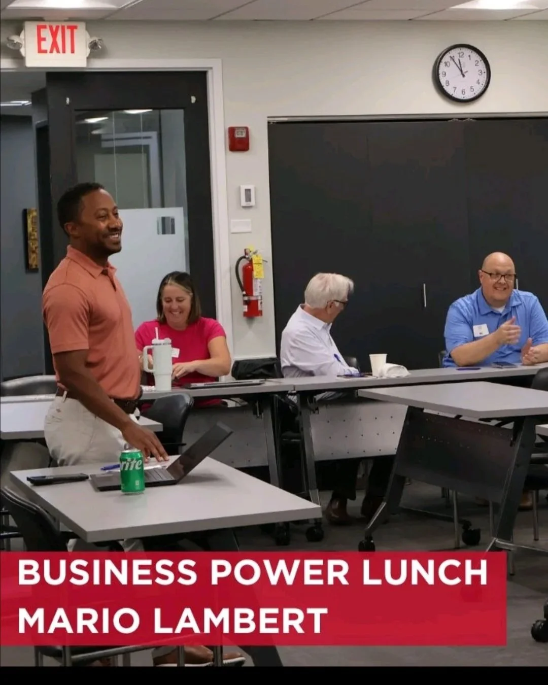 A group of four people sitting around a table in a conference room, with one person standing. The text overlay reads 'Business Power Lunch Mario Lambert'.