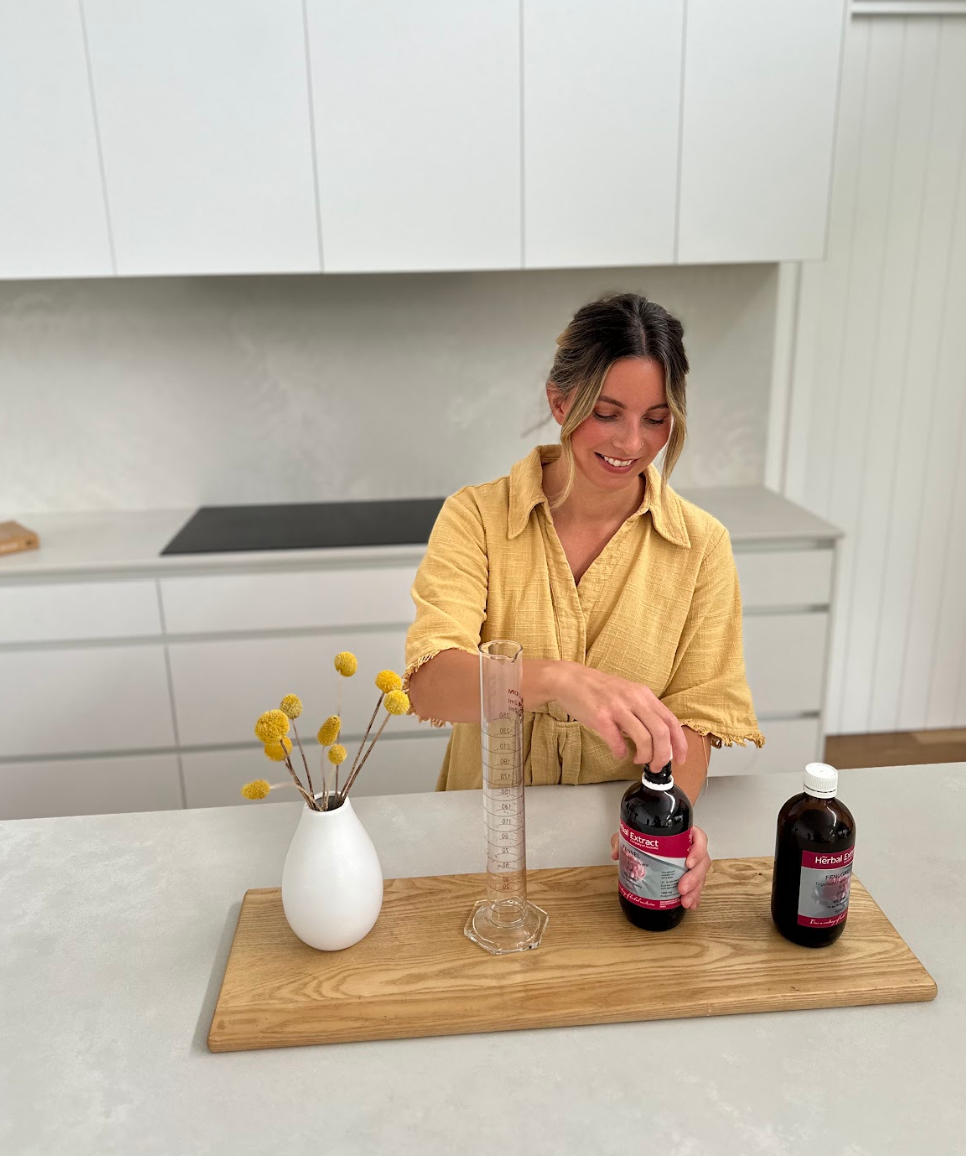 Woman in a yellow shirt preparing herbal extract bottles on a wooden tray in a modern kitchen.