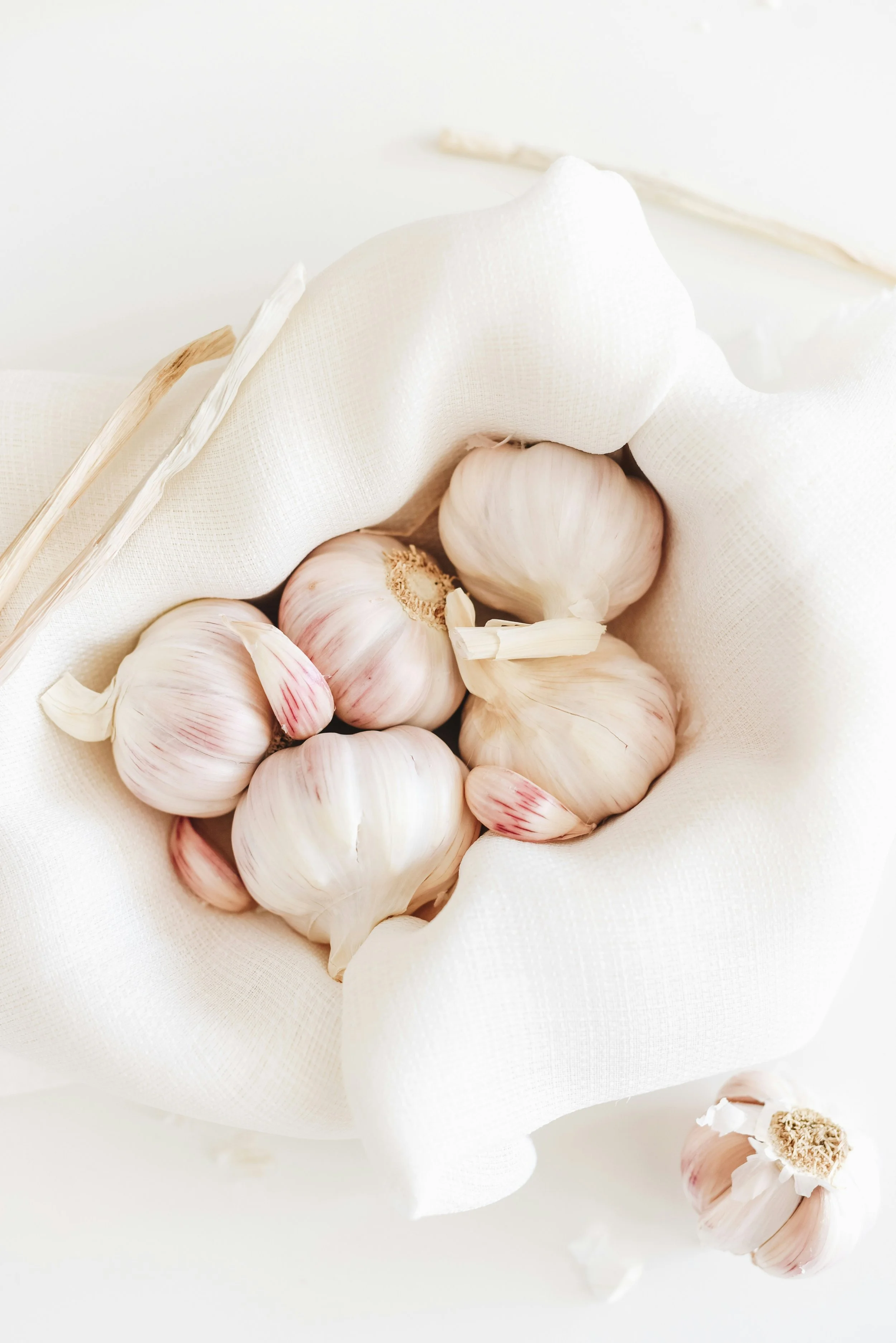 A bunch of whole garlic bulbs with some separated garlic cloves on a white fabric surface.