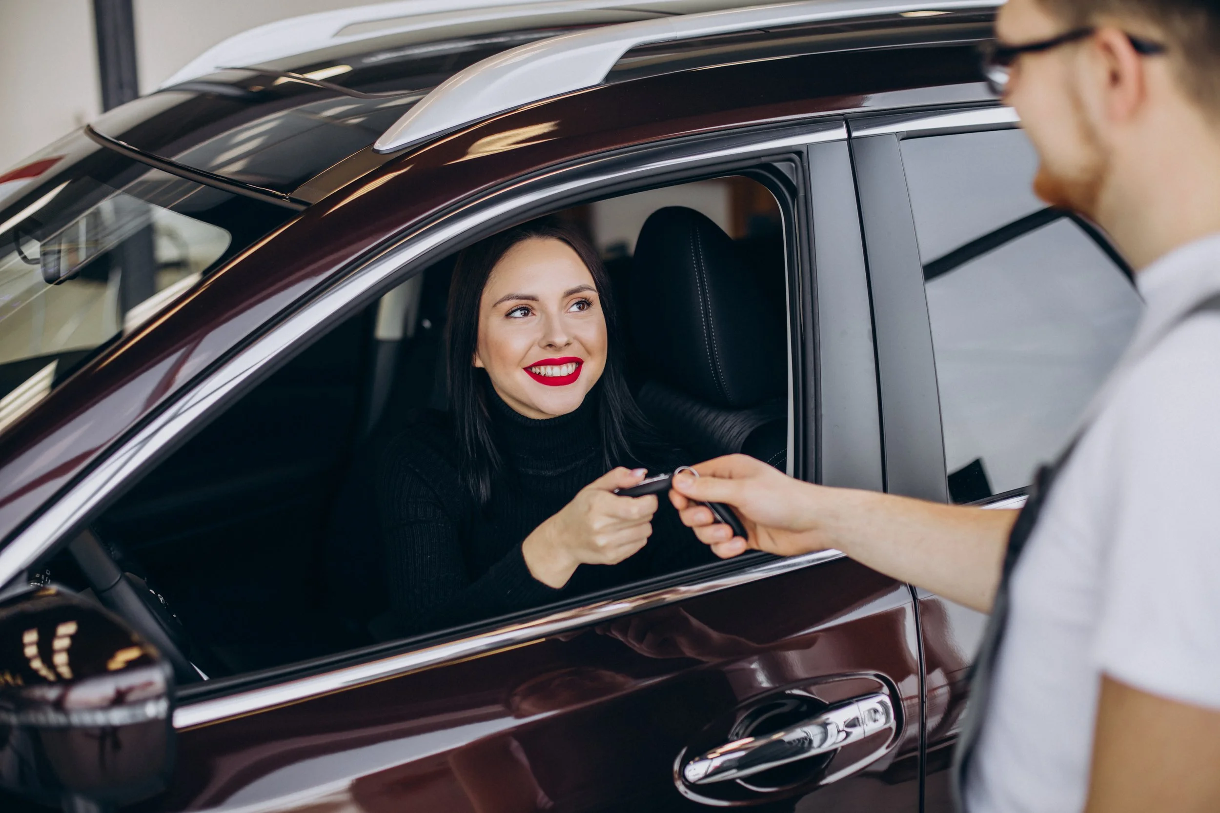 A woman in a black turtleneck smiling and hand to receive car keys from a man in a white shirt.