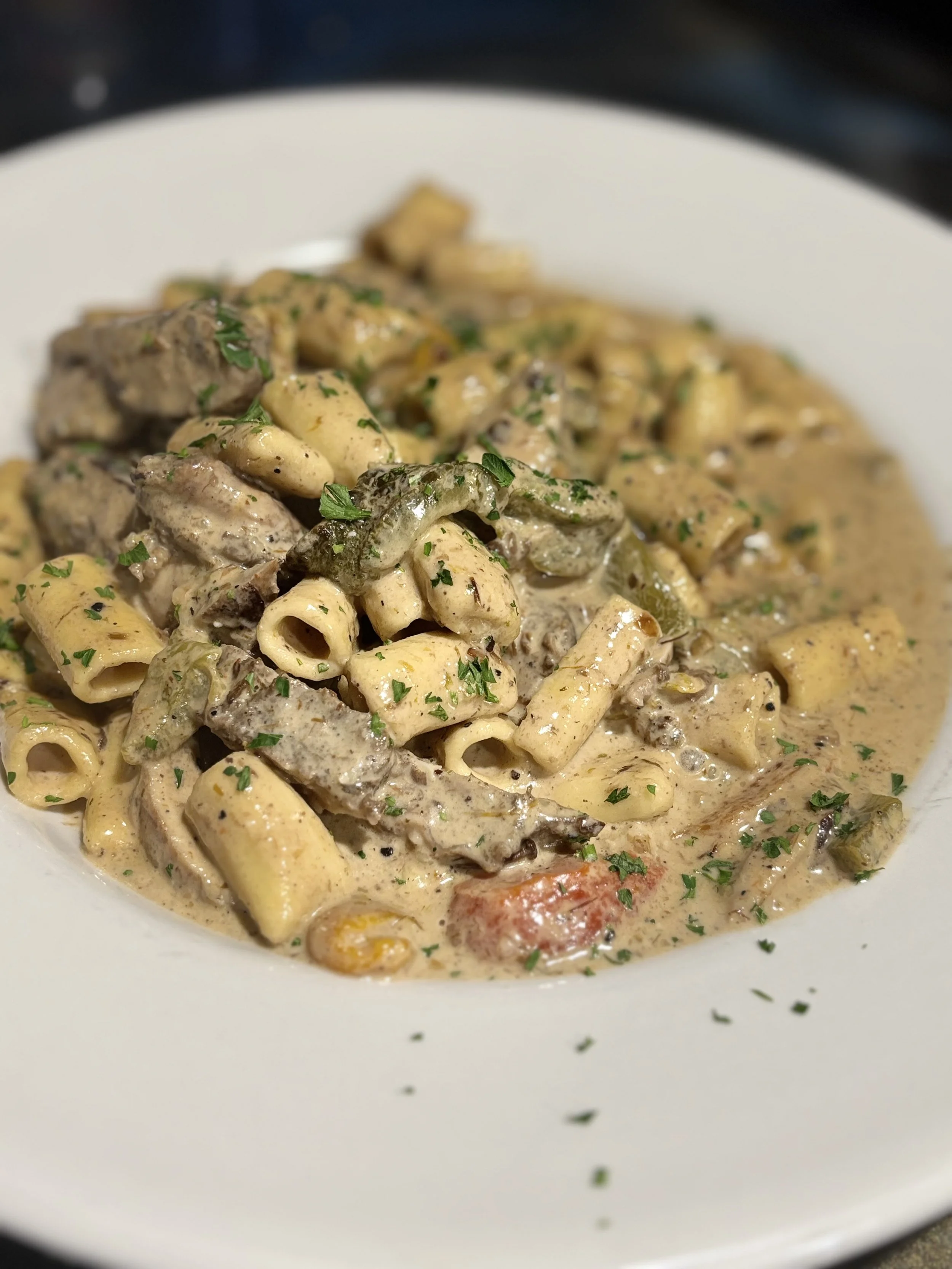 A bowl of creamy pasta with chunks of beef, vegetables, and herbs garnished with parsley.
