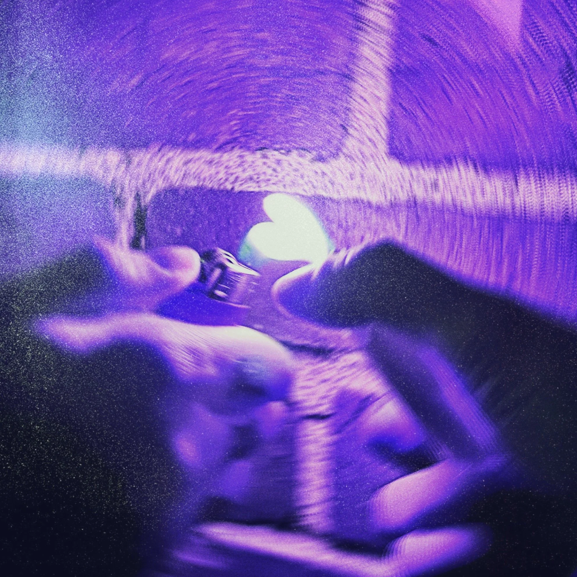 Close-up of two people holding lighters together to make a glowing flame heart-shaped light against a purple brick wall.