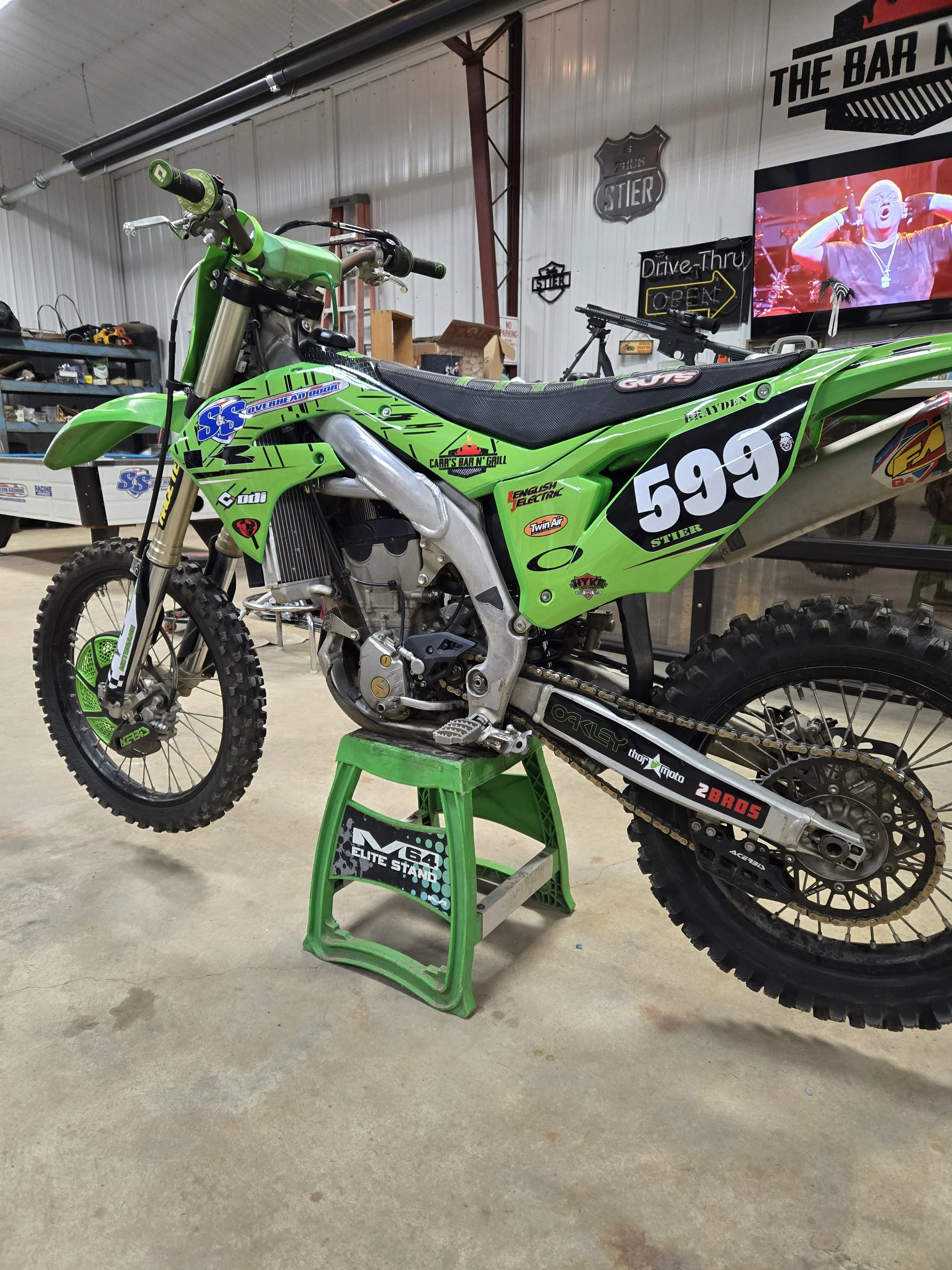 Green off-road dirt bike number 599 on a green stand in a workshop or garage.