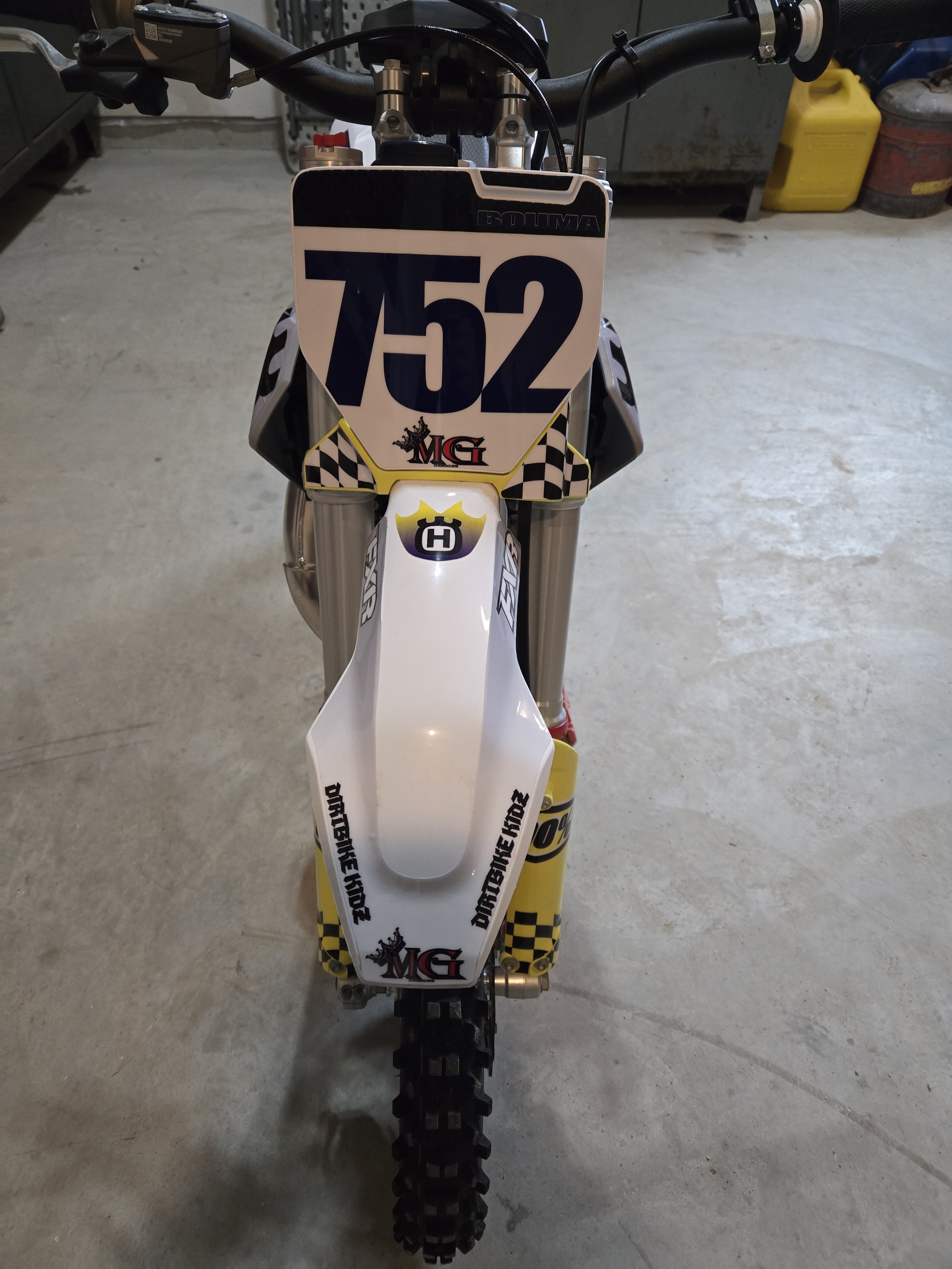 Front view of a dirt bike with a large white number plate displaying the number 752, various sponsor stickers, and knobby off-road tires, parked on a concrete floor in a garage.