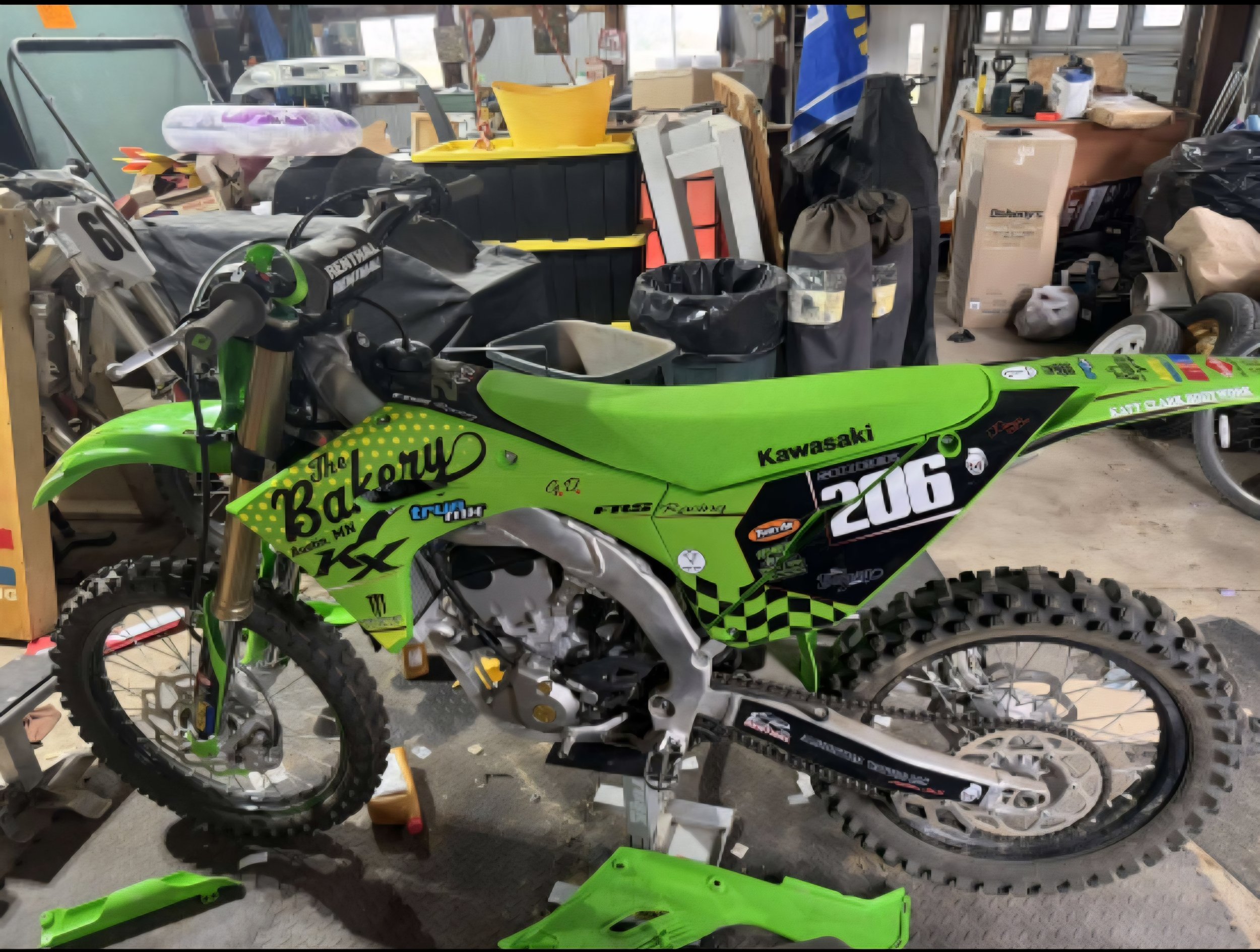 Green Kawasaki dirt bike with racing decals and the number 206, in a cluttered garage or workshop.