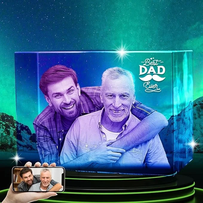 Two men, one older with gray hair and the other younger with brown hair, smile and embrace each other in front of a backdrop with starry sky and northern lights. A sign reads 'Best Dad Ever.'