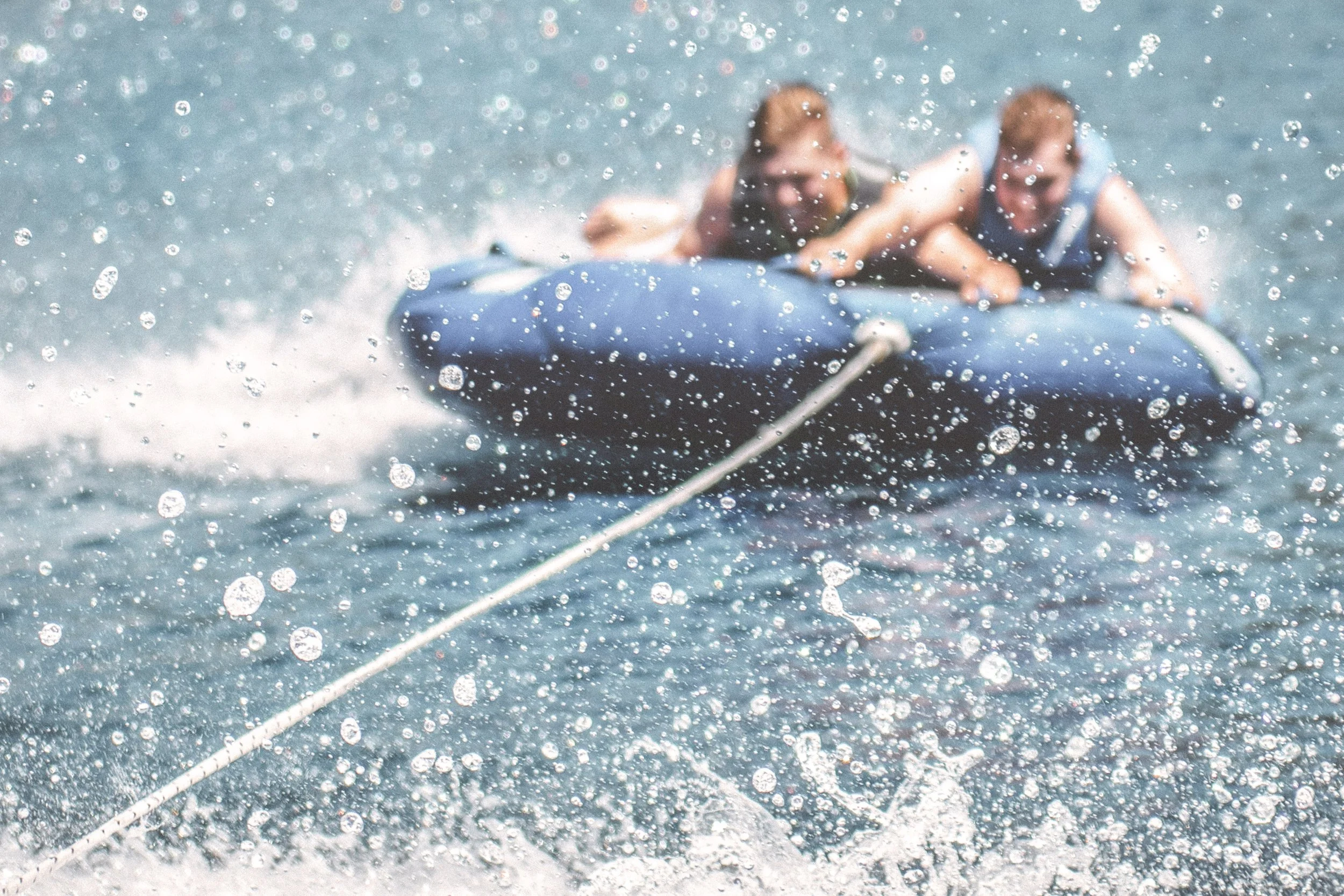 Two teenage boys tubing from a boat in a lake at a family lake house while on vacation.
