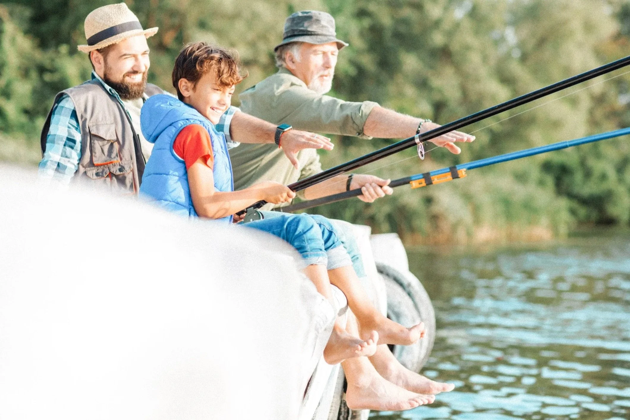 Grandfather, father, and grandson fishing together at a family lake house during vacation and pointing to the fish while safely sitting on the dock.