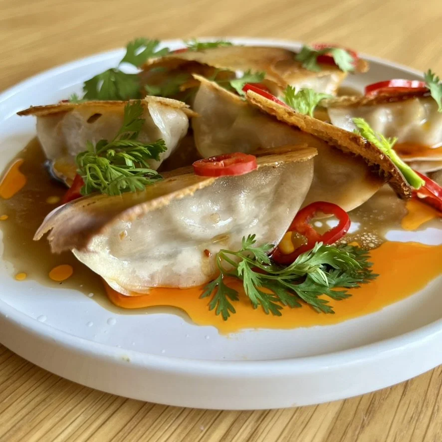 Plate of Chinese dumplings topped with sliced red chilies, fresh cilantro, and green onions, served with soy sauce and chili oil.