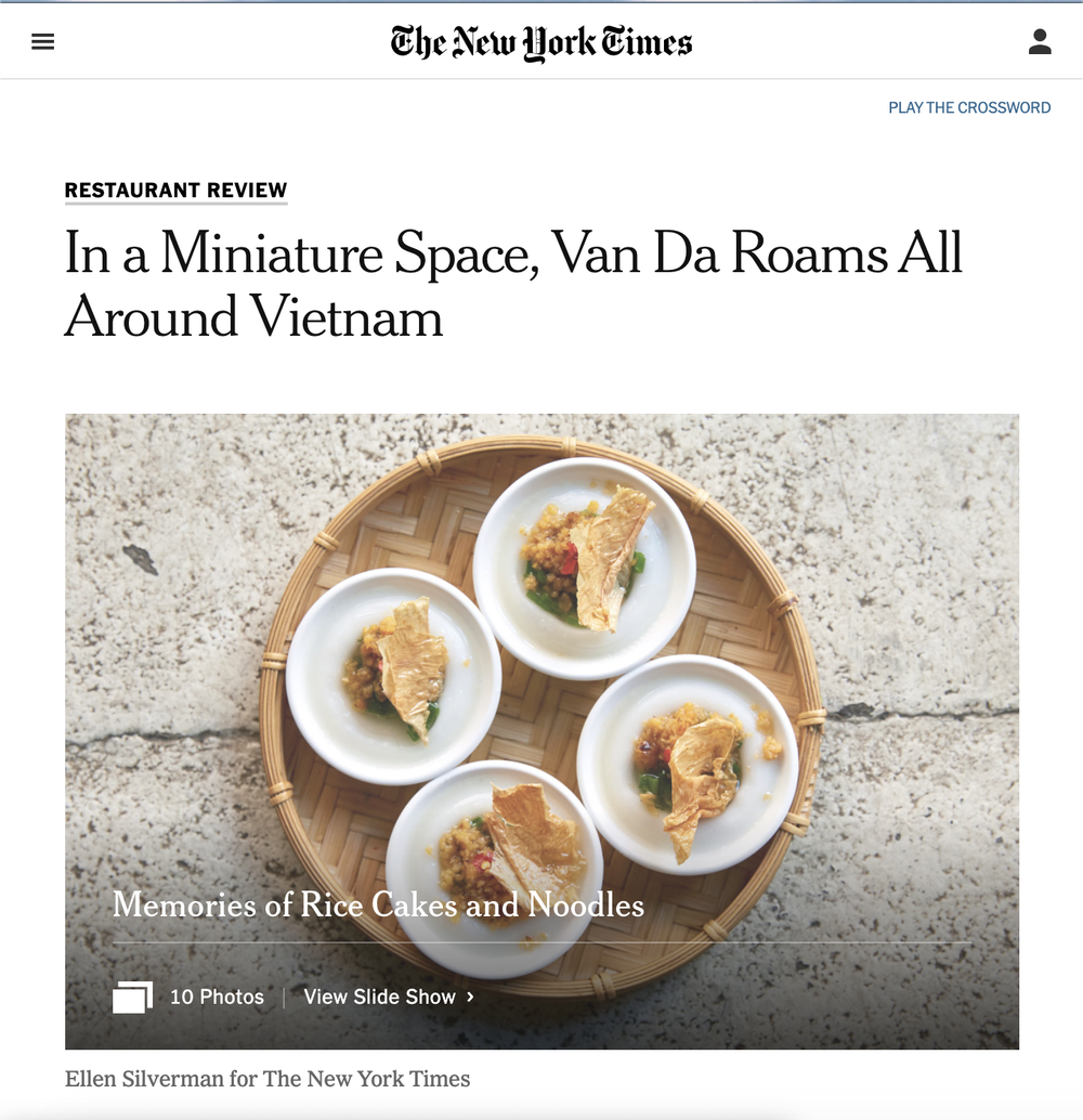 Four small white bowls with rice cakes and noodles on a round wicker tray, viewed from above, placed on a stone surface.