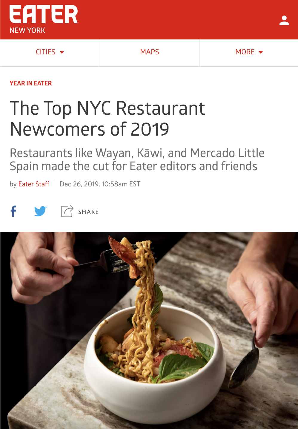 A person is holding a fork with a portion of noodles and a piece of bacon over a white bowl filled with noodles, seafood, and fresh basil leaves on a kitchen counter.