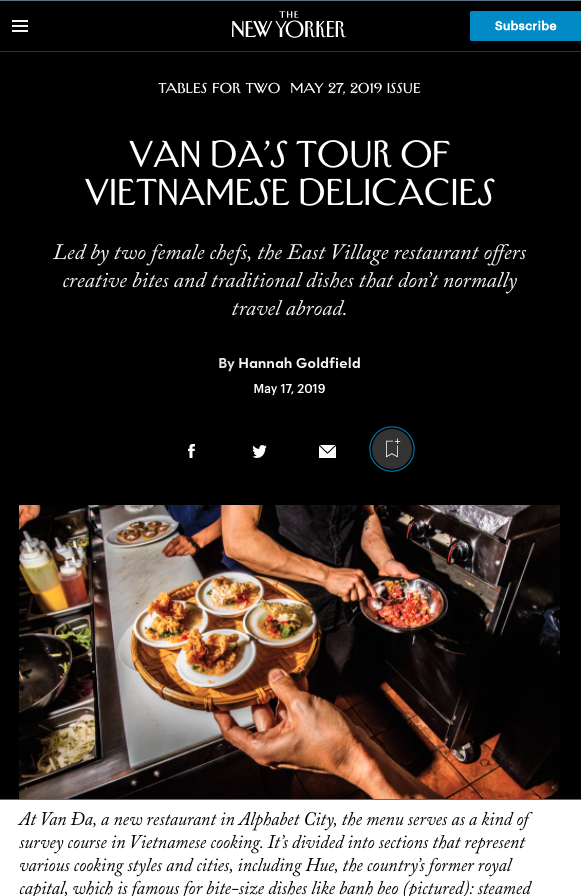 A person holding a wooden tray with several plates of Vietnamese dishes, with another person cooking in a kitchen in the background. New York Times article featuring Hannah Wong.