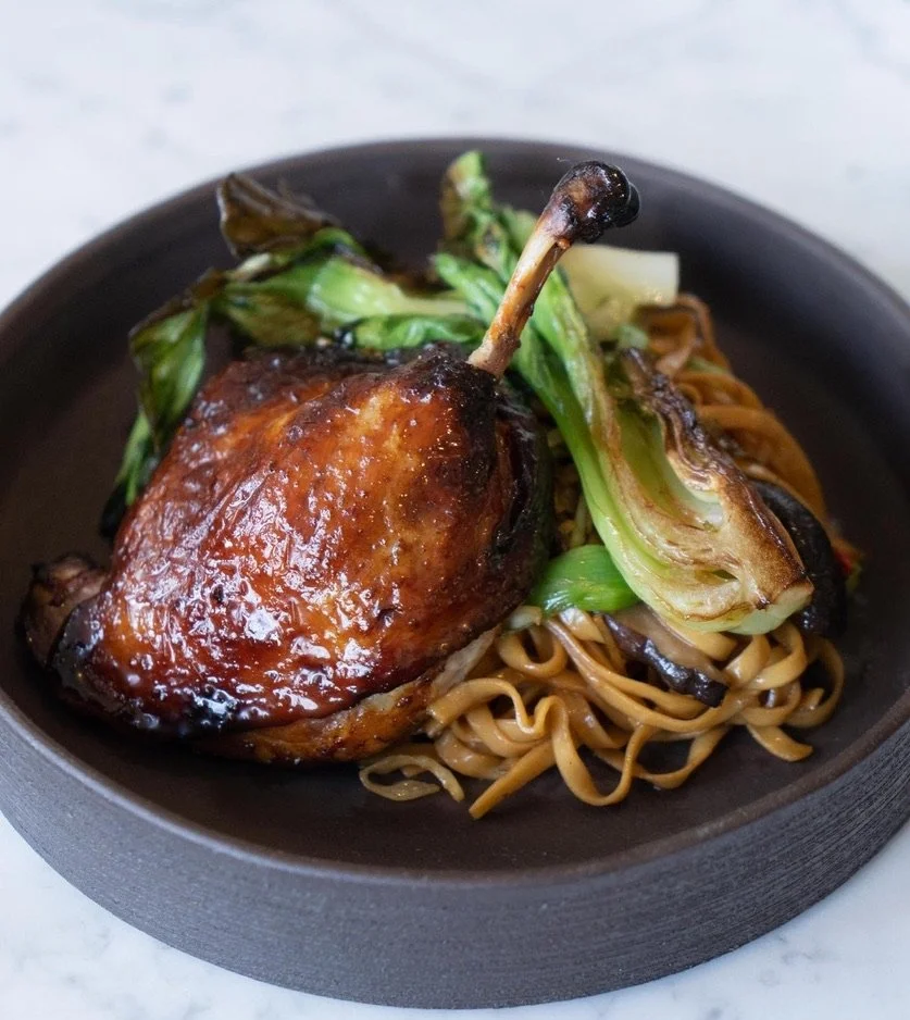 Roasted duck leg with grilled vegetables and noodles on a black plate