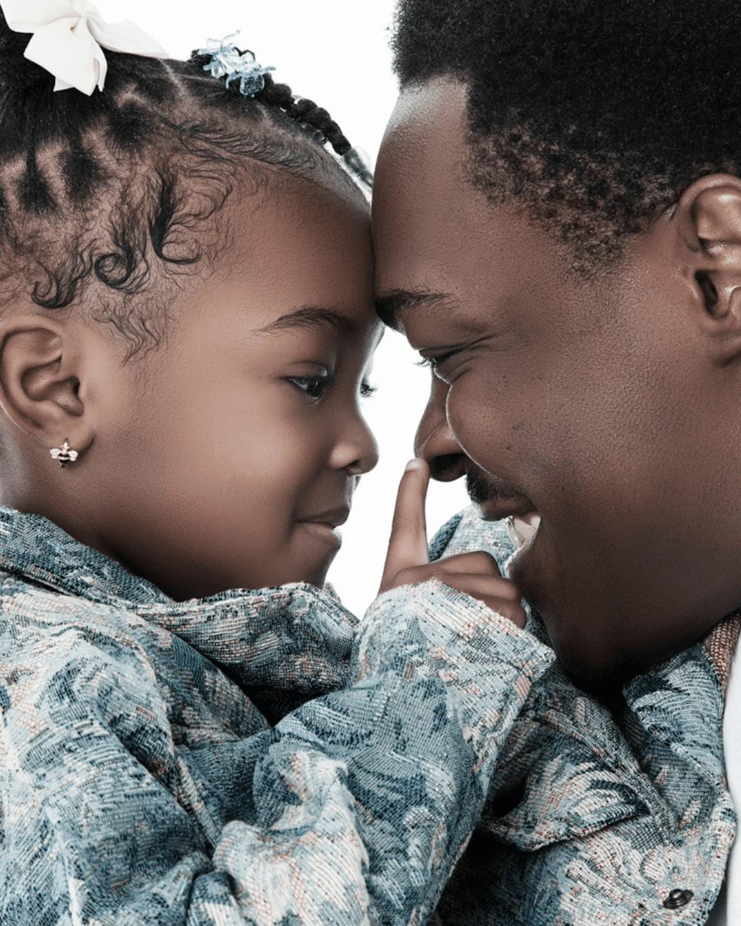 A father and daughter with foreheads touching, smiling, and eyes closed, sharing a tender moment.