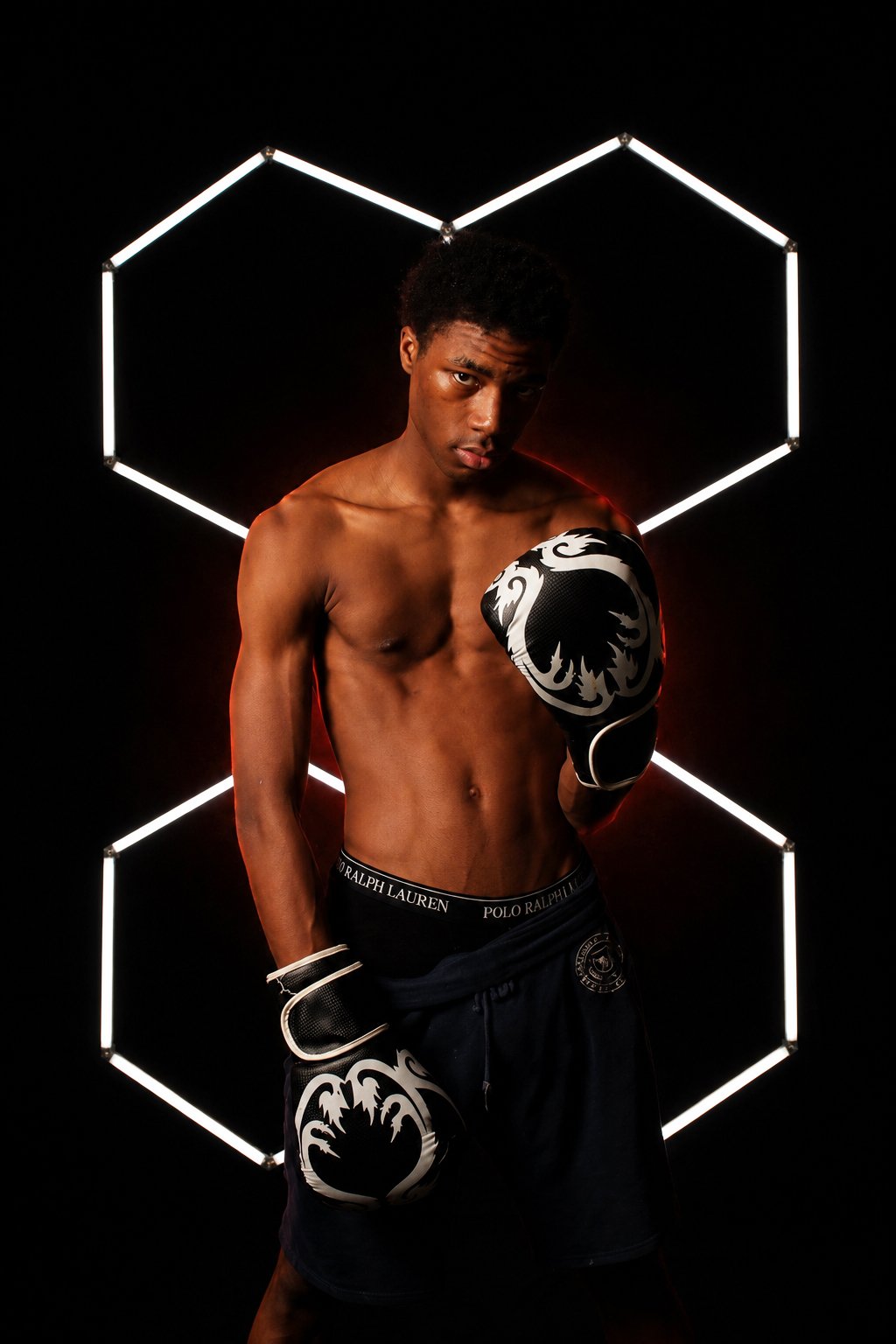 A shirtless boxer with gloves in front of a black background with illuminated geometric shapes.