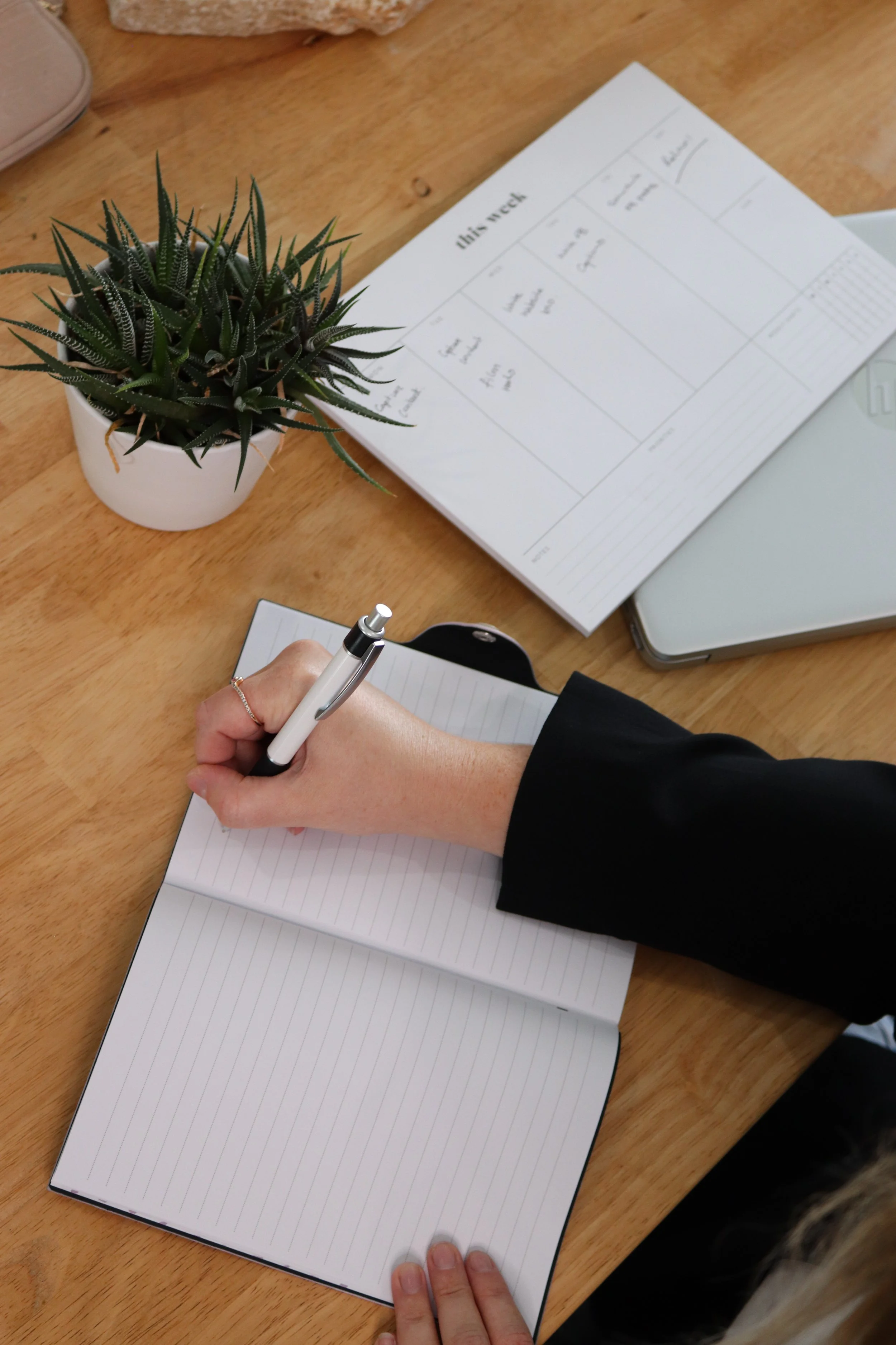 A woman's hand holding a white and black pen writing on a notebook.